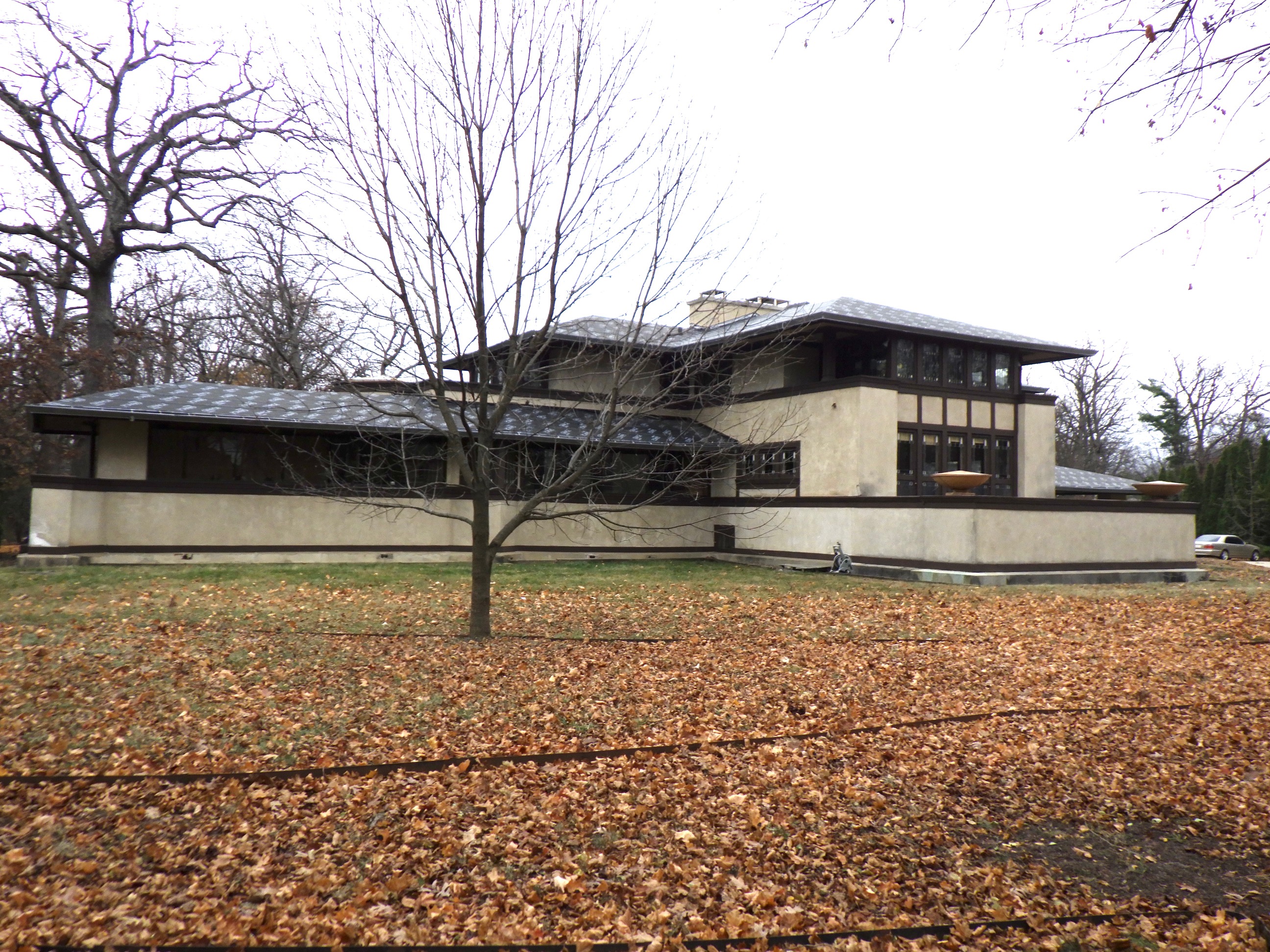Prairie-style house with horizontal lines, wide eaves, and dark trim amid bare trees.