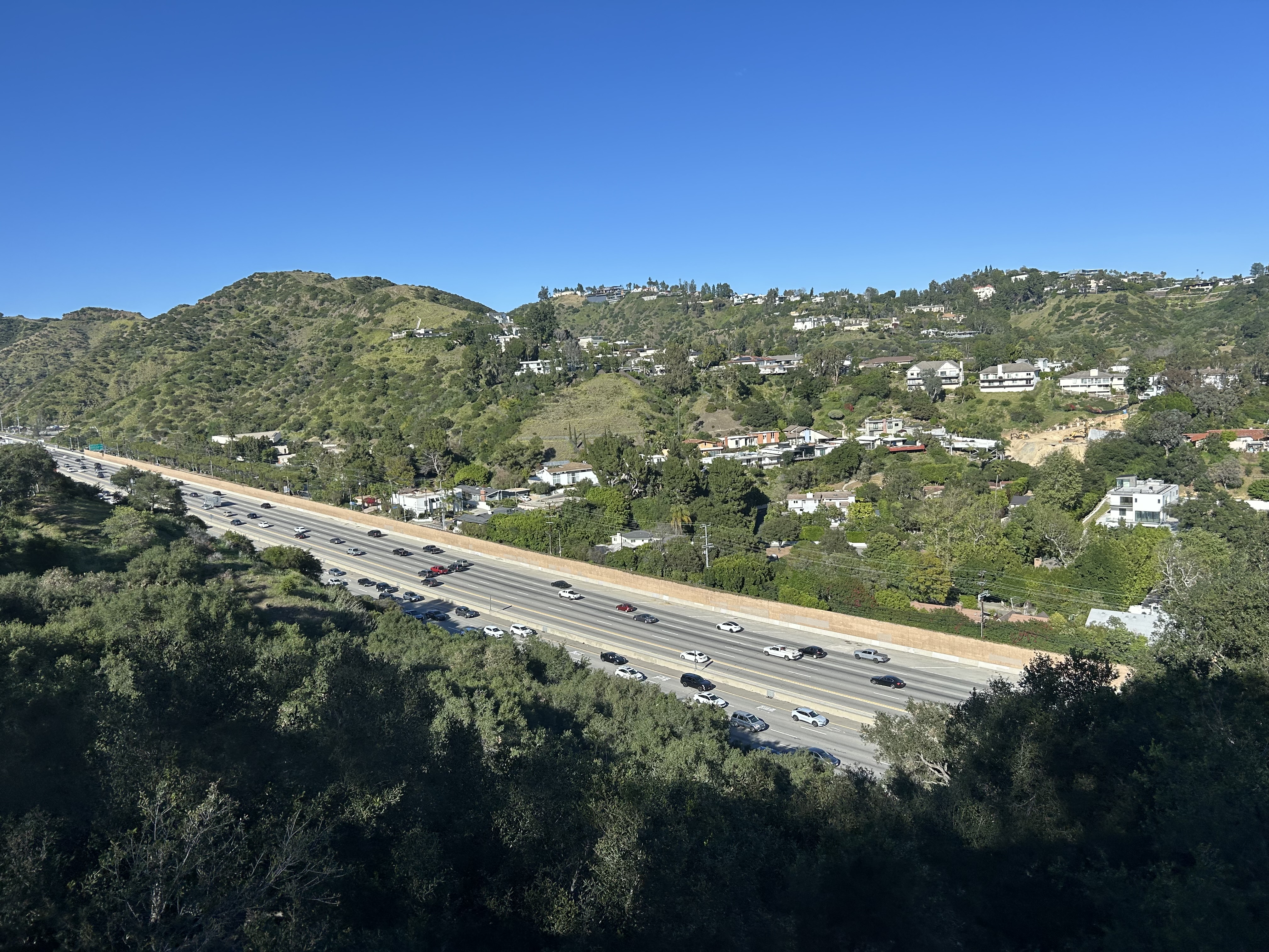 Multi-lane freeway cutting through green hillsides with traffic in both directions.