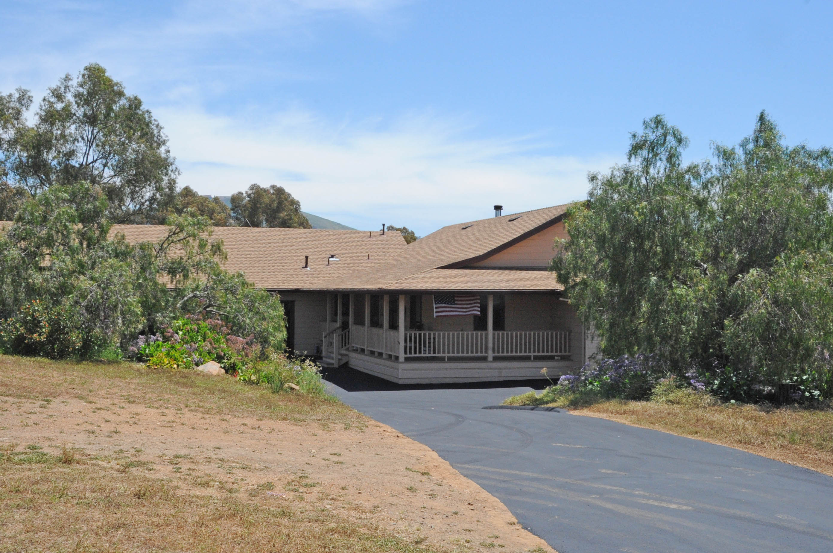 Single-story ranch house with a covered porch and American flag, surrounded by eucalyptus trees.