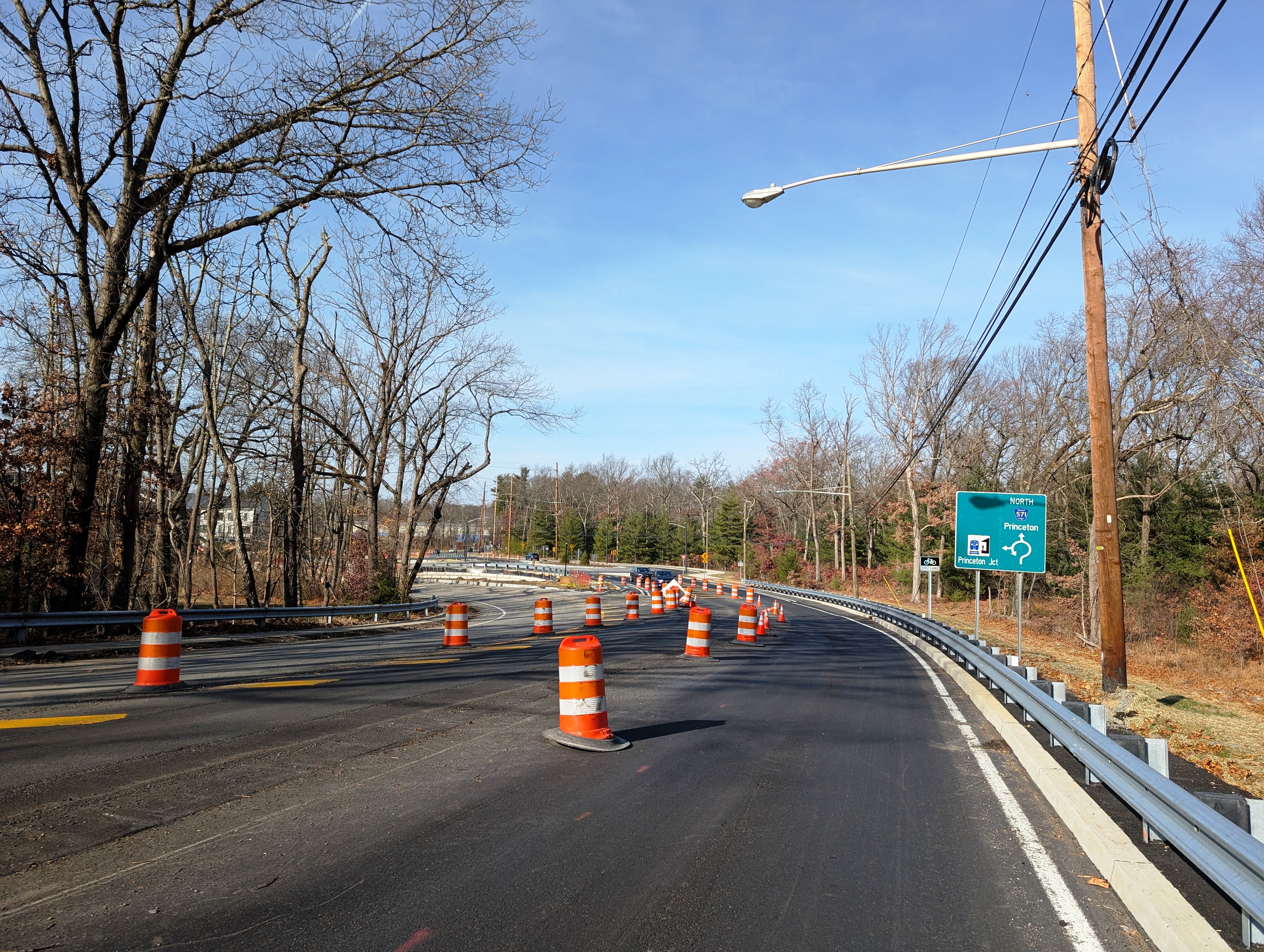 Orange traffic barrels line a two-lane road under construction beneath a clear blue sky.