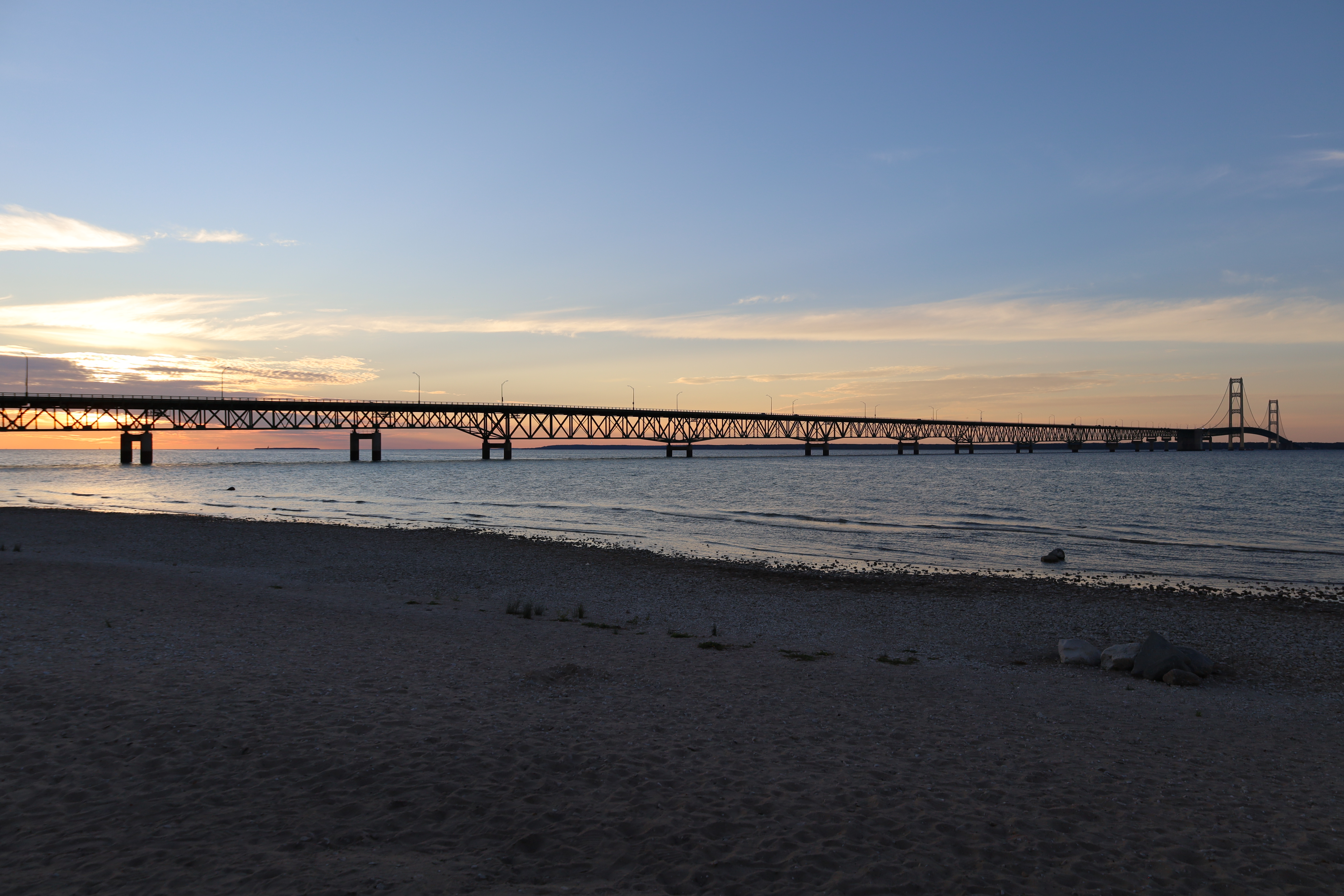 Suspension bridge silhouetted against a colorful dusk sky over calm water.