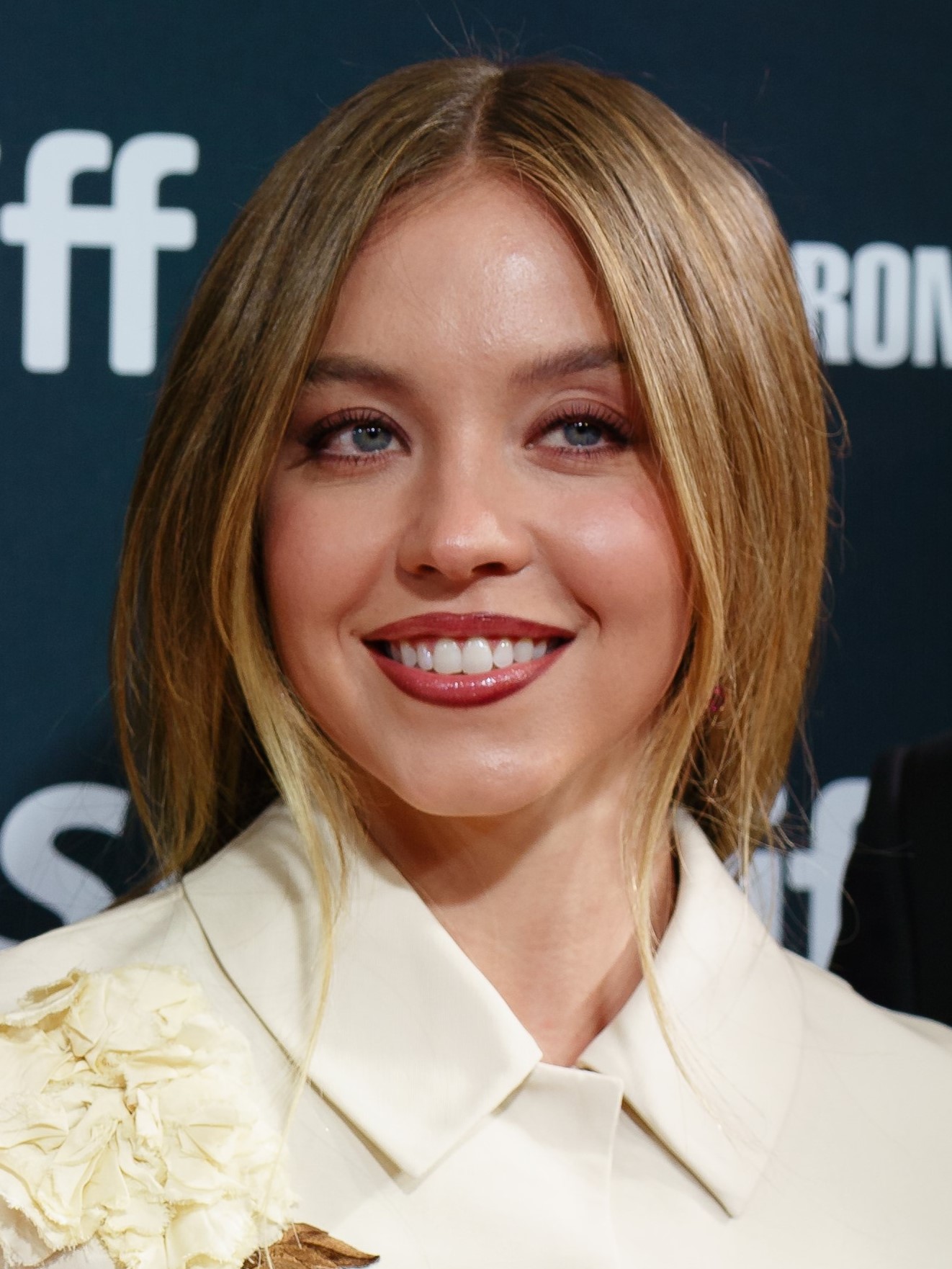 Blonde woman in a cream floral jacket smiling at a film festival backdrop.