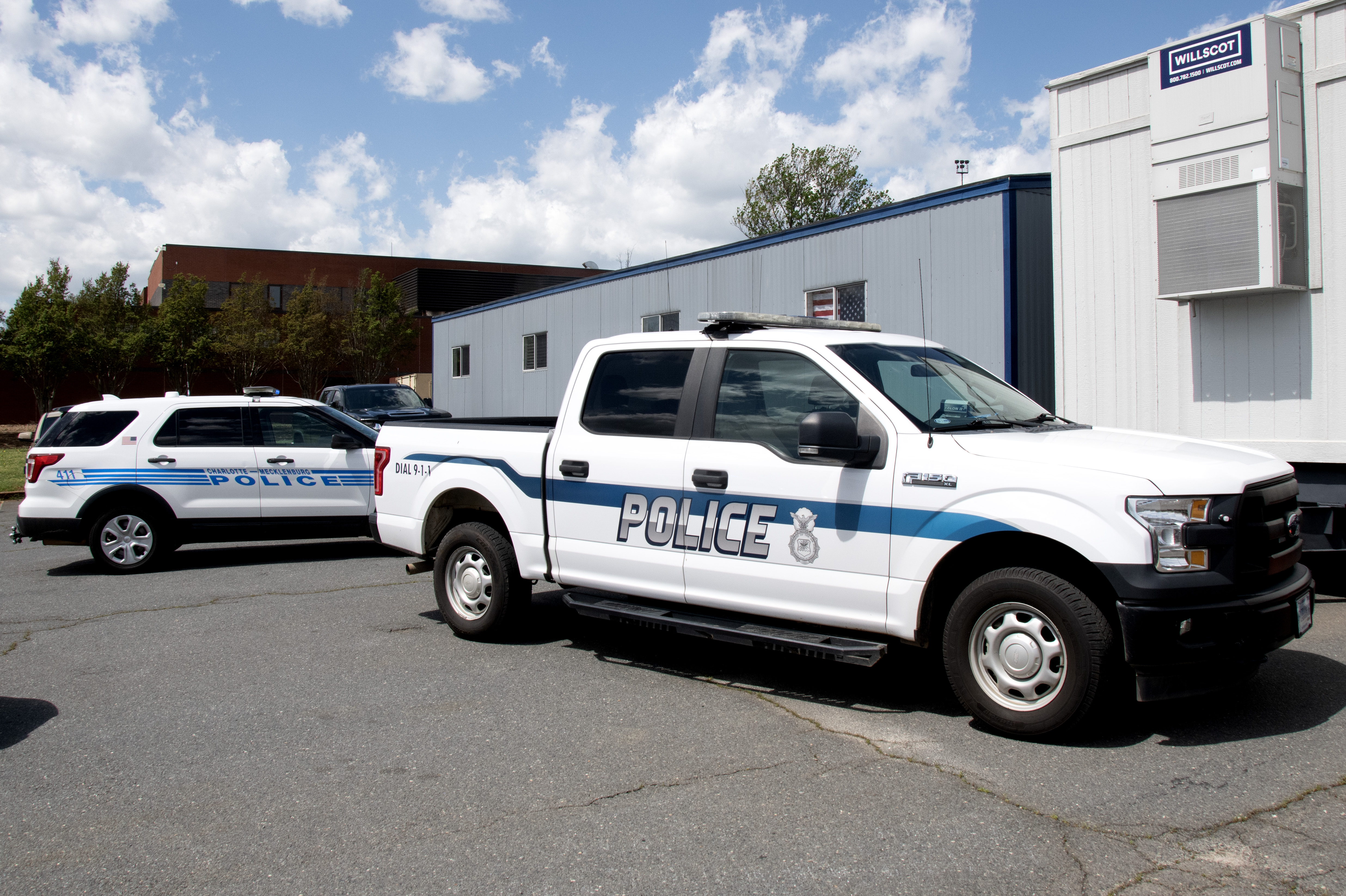 Two white CMPD police vehicles parked in a lot under a blue sky.