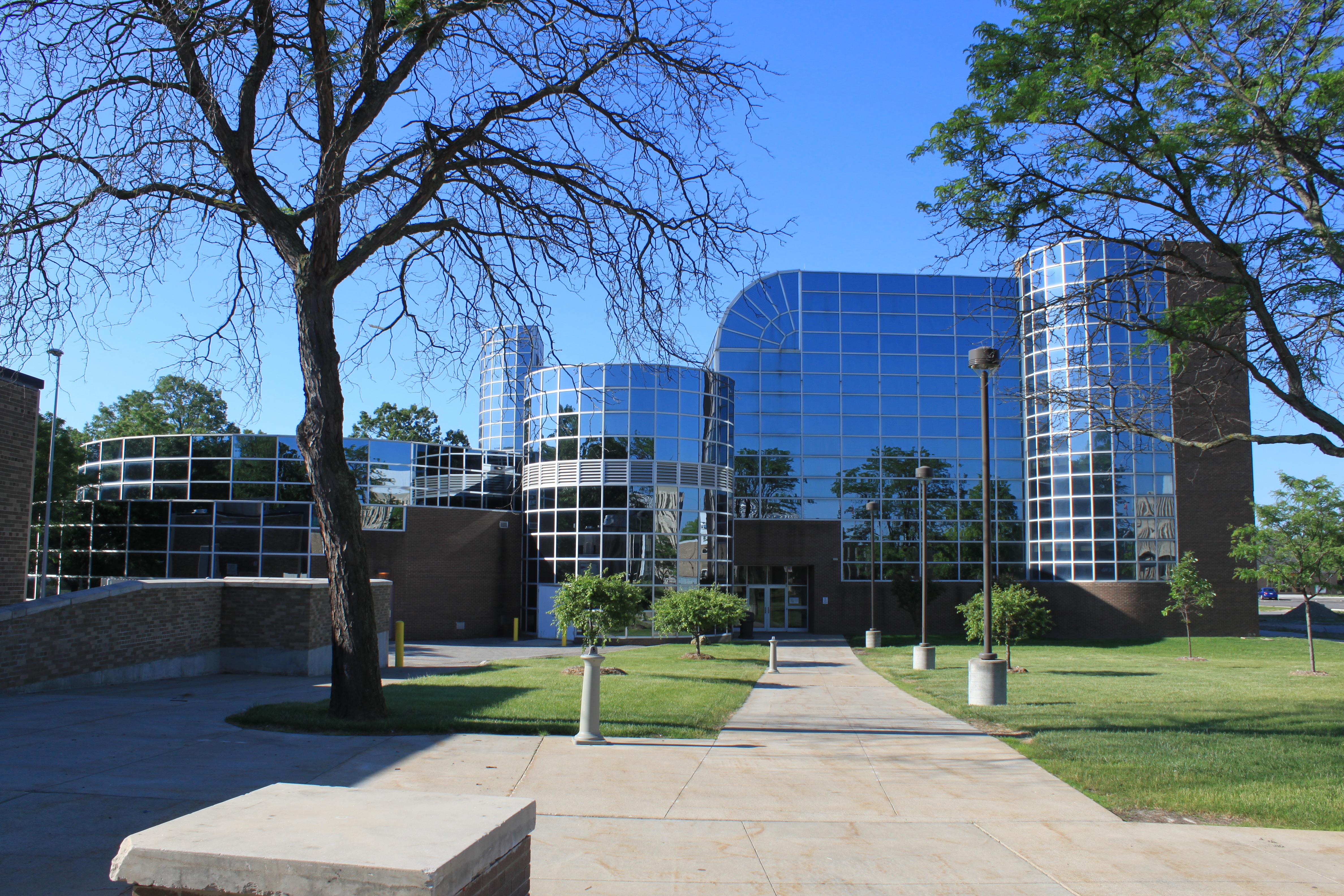Modern glass-and-steel college building with curved towers and blue reflective panels on a sunny day.