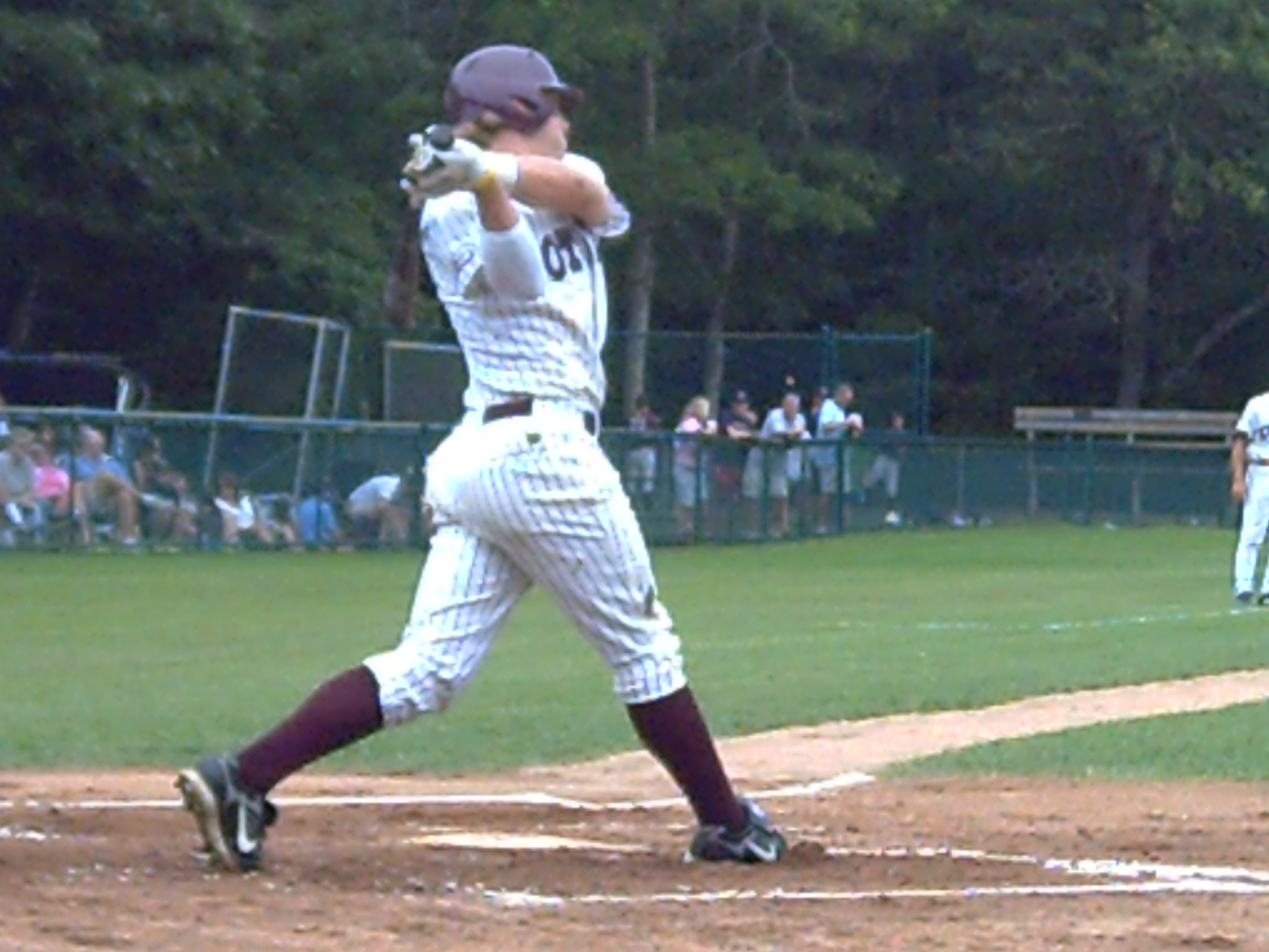 A baseball batter in a white pinstripe uniform completing a full swing at home plate.