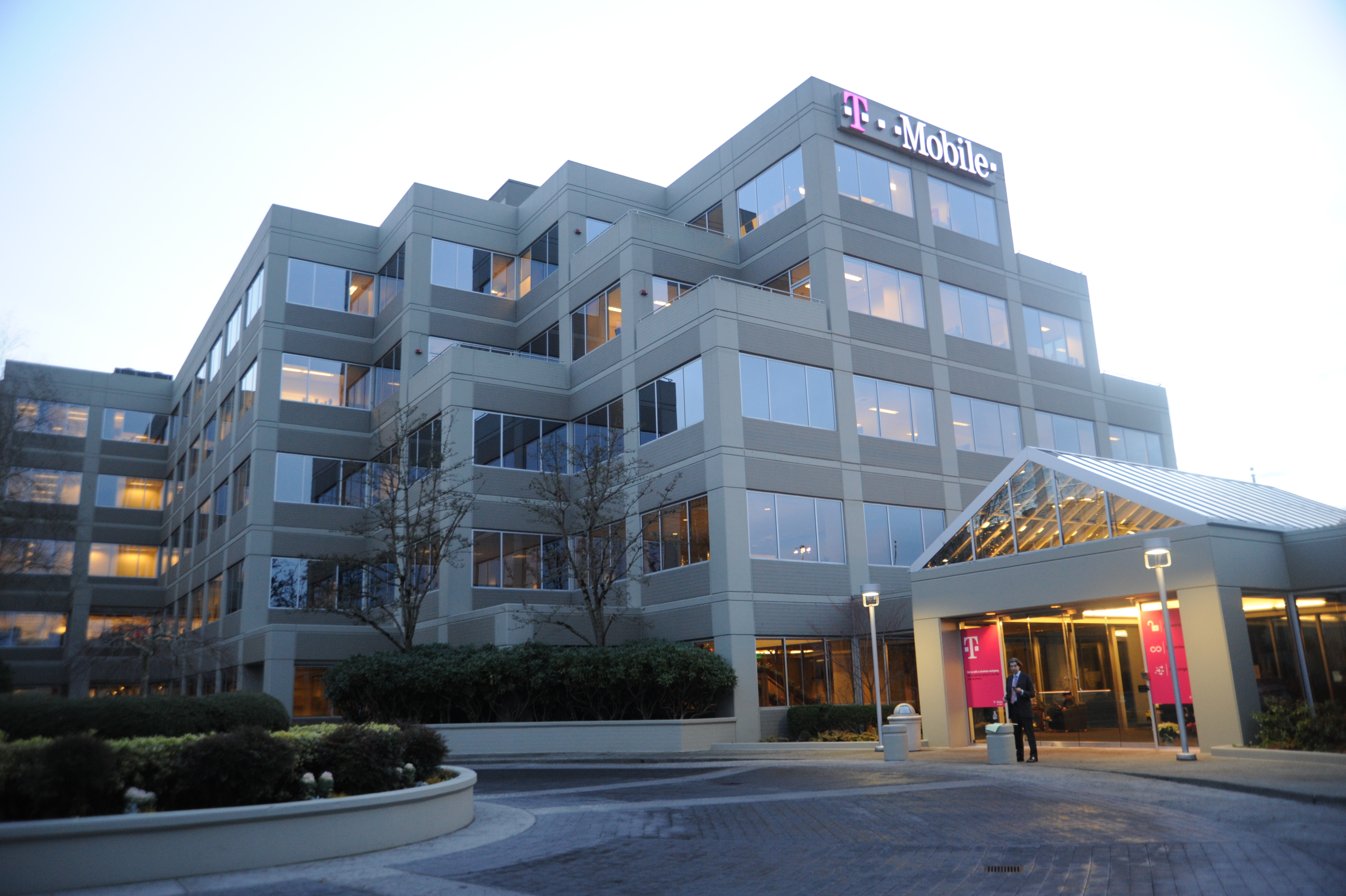 Multi-story glass office building at dusk with a T-Mobile logo on the upper facade and a lit entrance canopy.