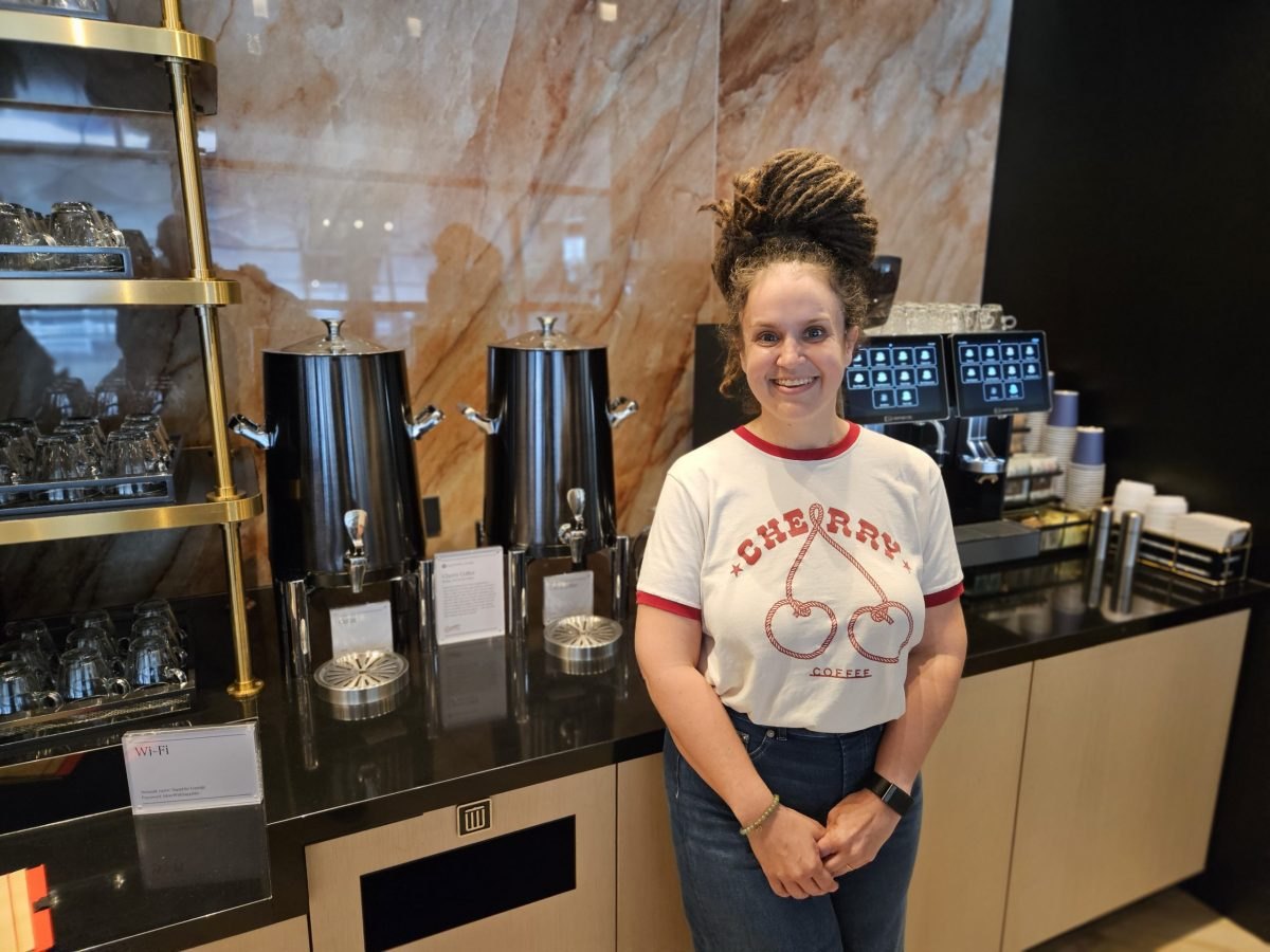 A smiling woman in a Cherry Coffee t-shirt stands at a modern espresso bar.