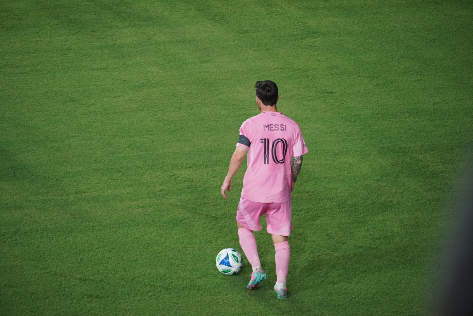 Soccer player in a pink jersey with number 10 on the back, ball at feet on grass.