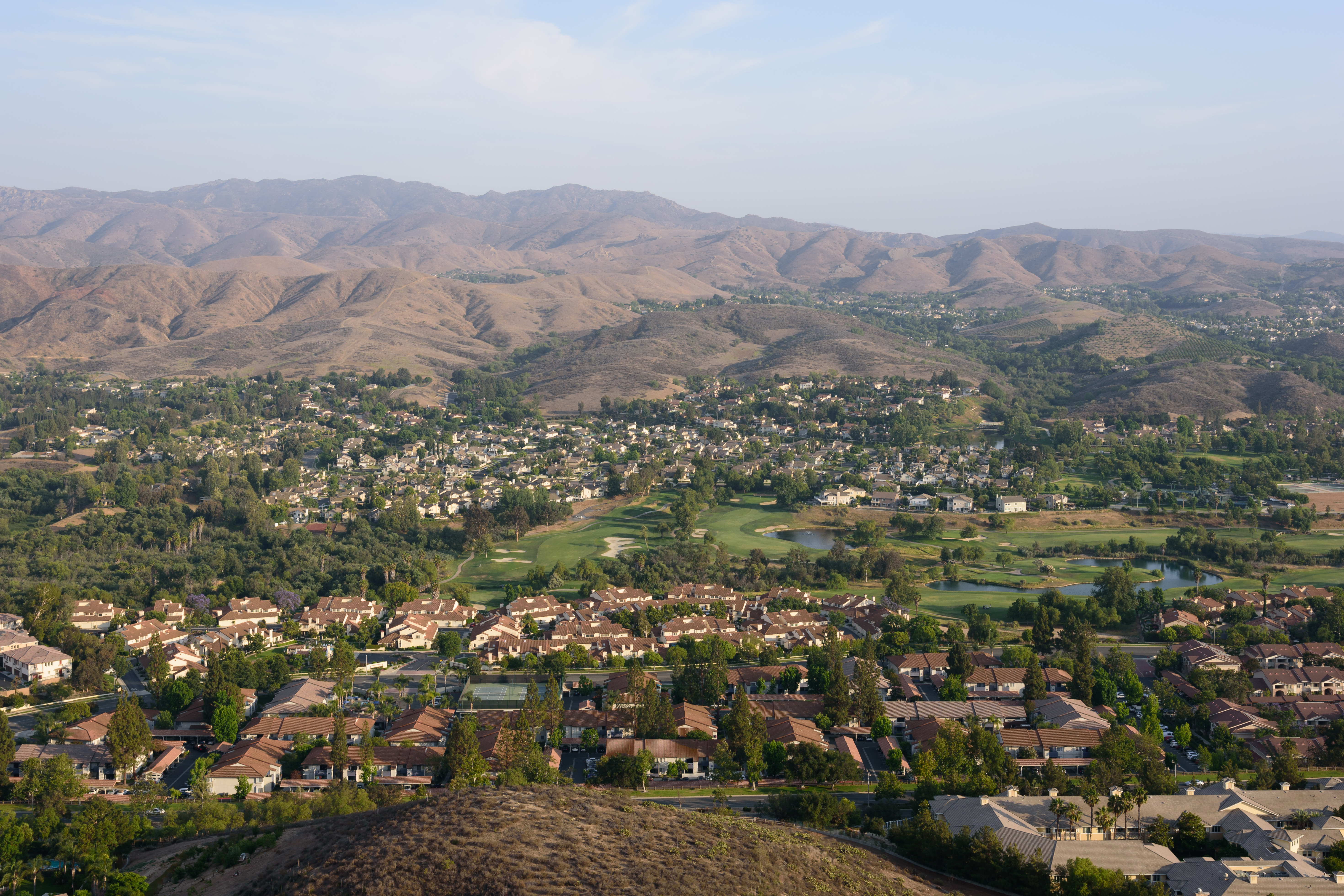 Aerial view of a golf course with green fairways surrounded by residential neighborhoods and hills.