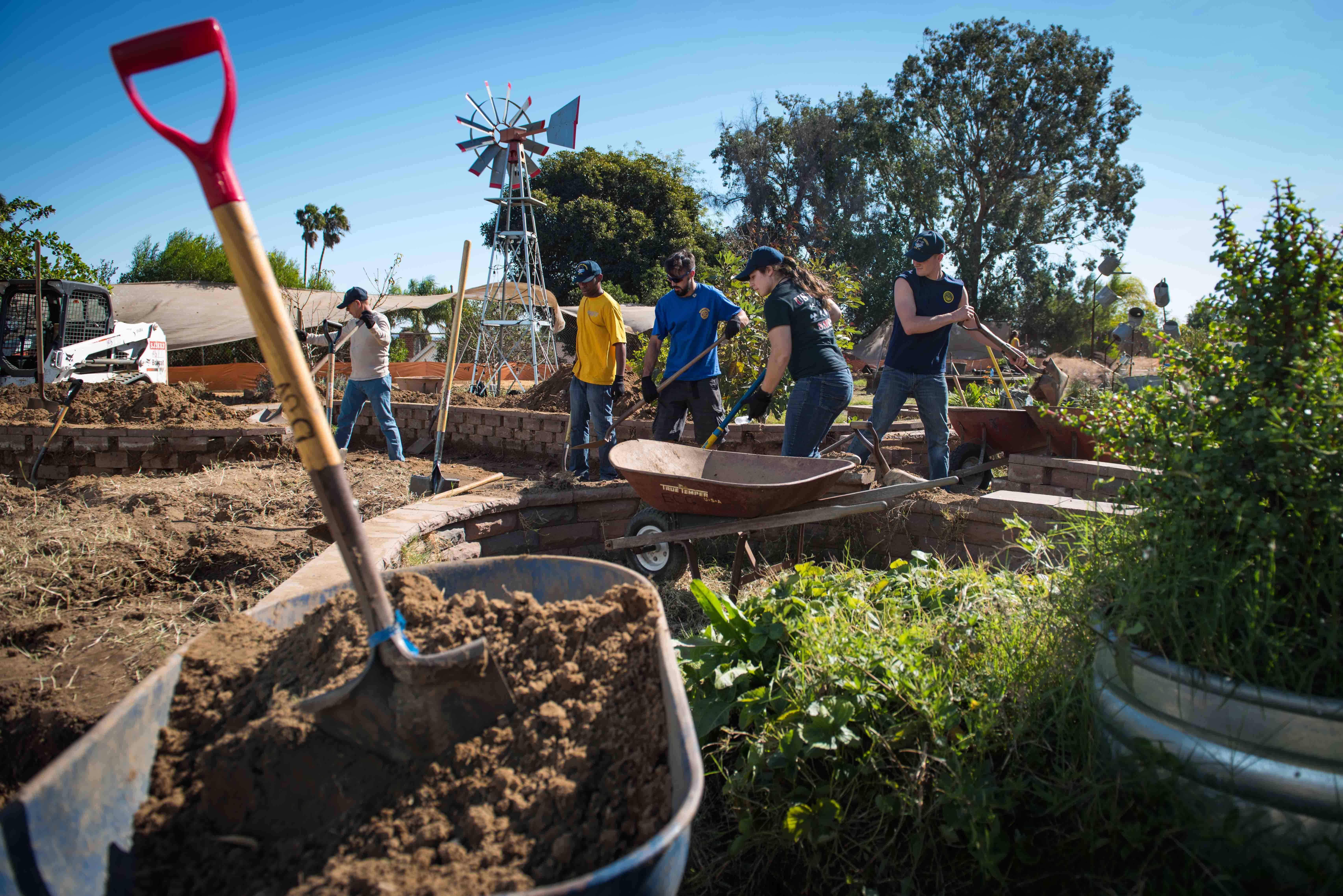 Volunteers with shovels and garden tools working in raised beds at an outdoor community event.
