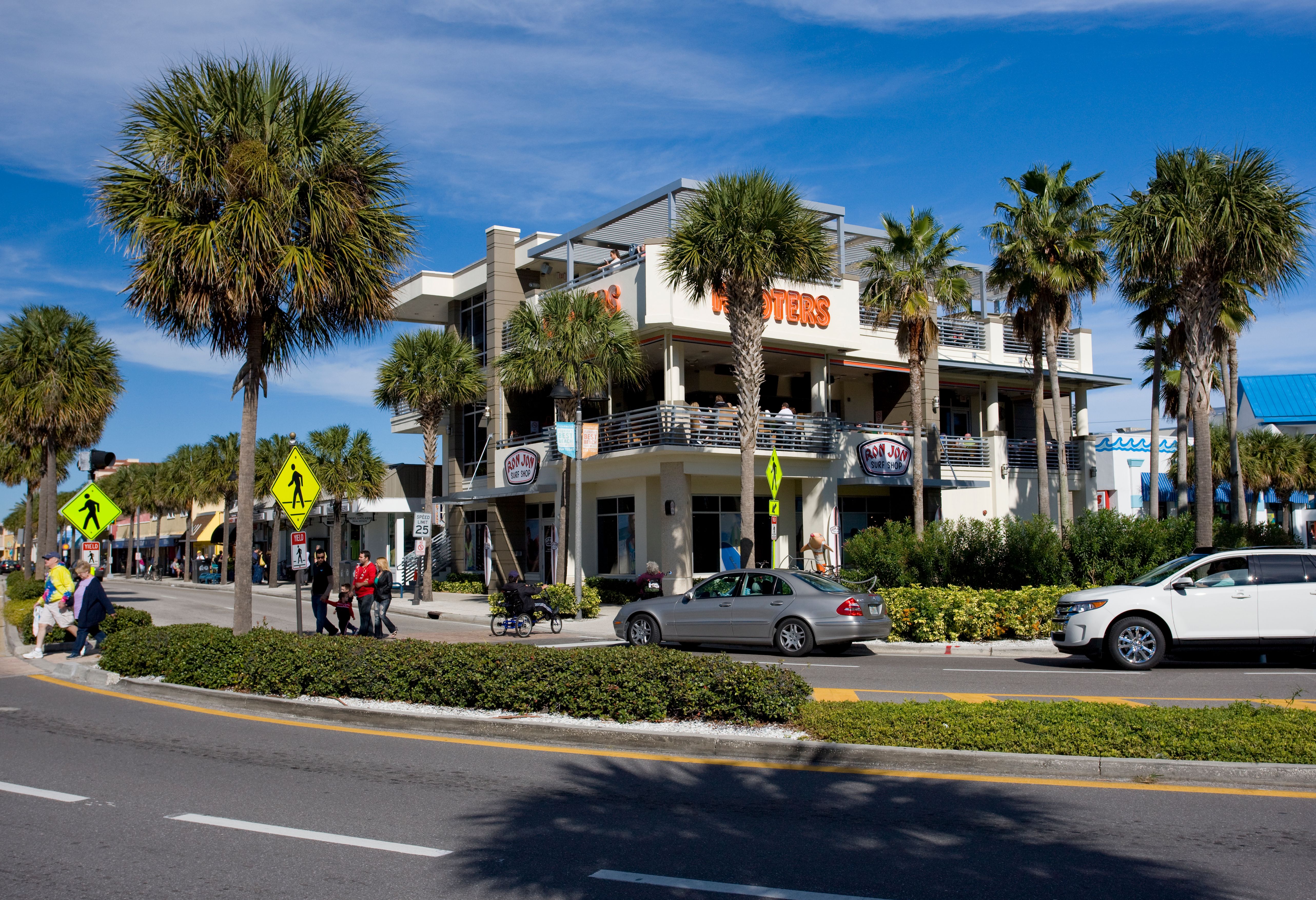 Multi-story restaurant building on a palm-lined street on a sunny day.