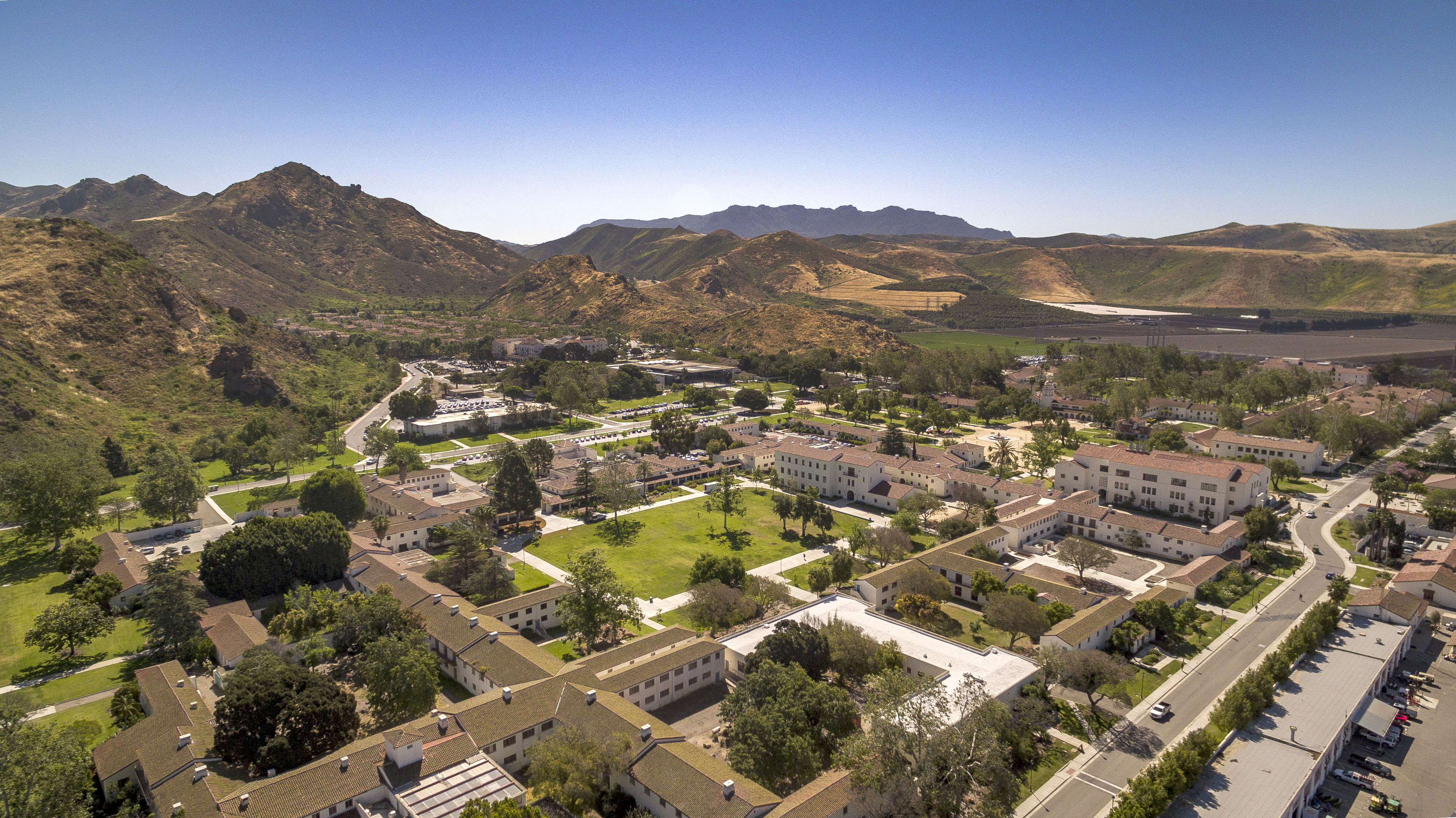 Aerial view of a university campus with red-tile roofs, green courtyards, and mountains behind.