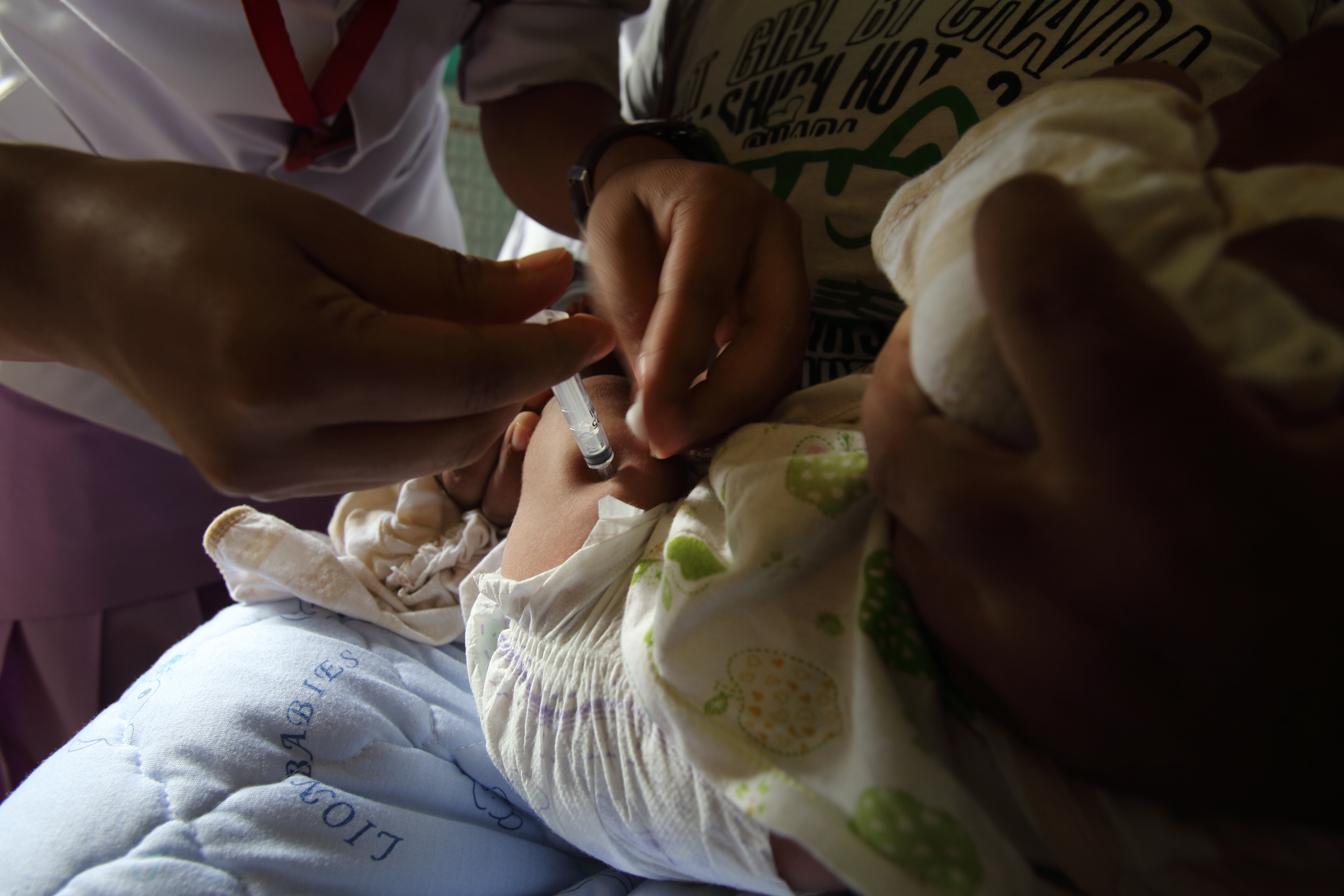 Healthcare worker in white gives a vaccine to an infant held by a caregiver.