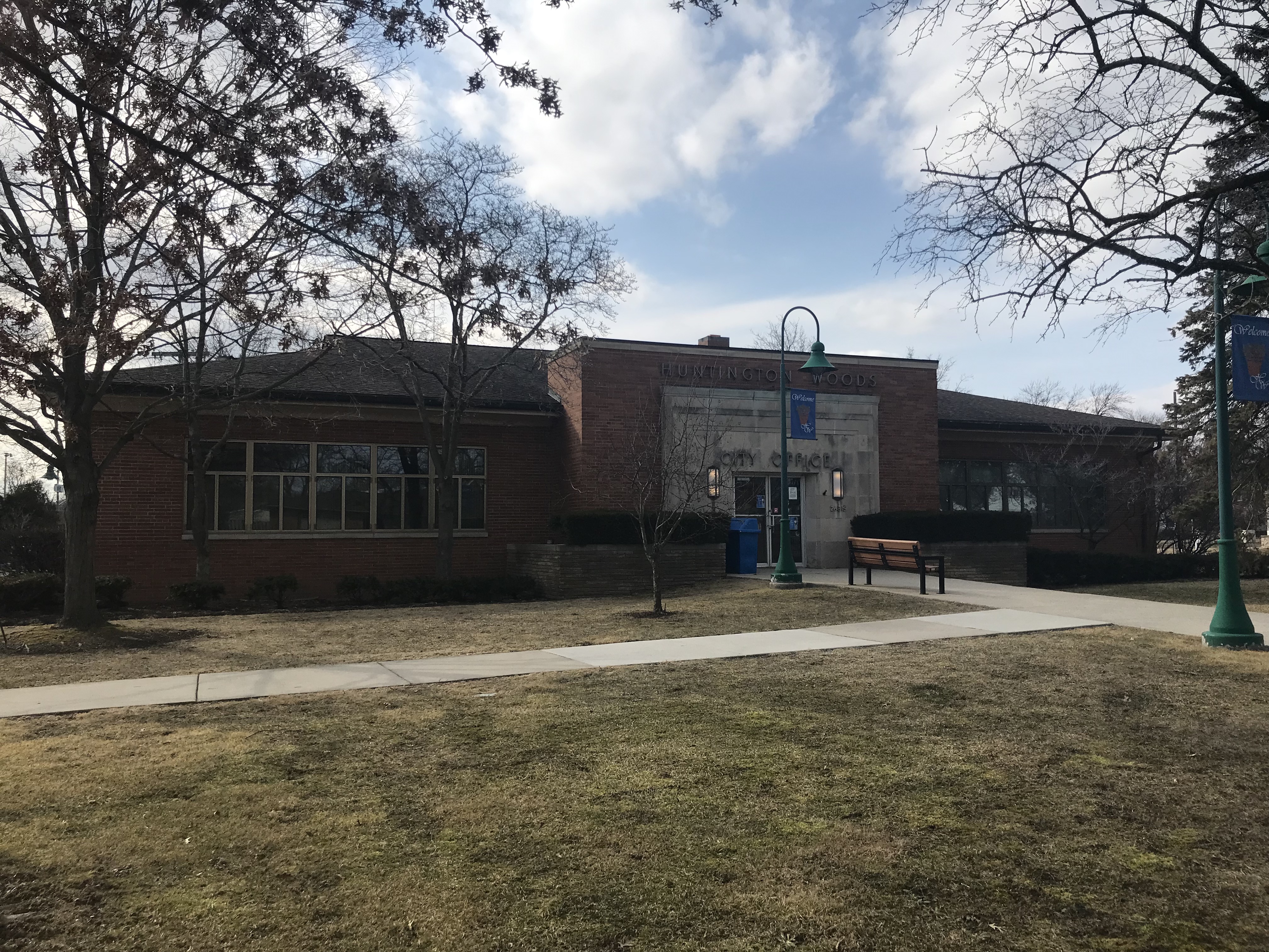 Single-story brick municipal building with large windows and a bench outside.