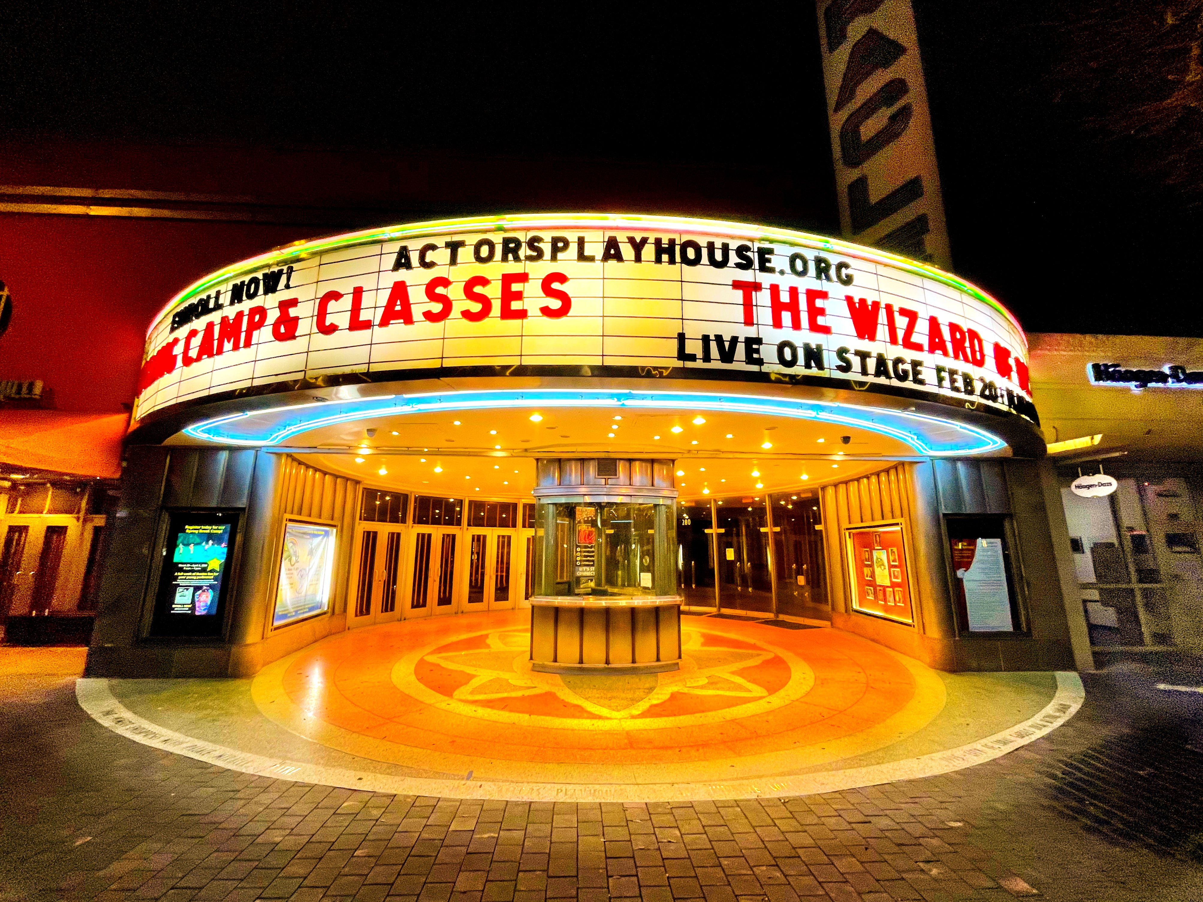 Illuminated Art Deco theater marquee glowing with teal and orange neon at night.
