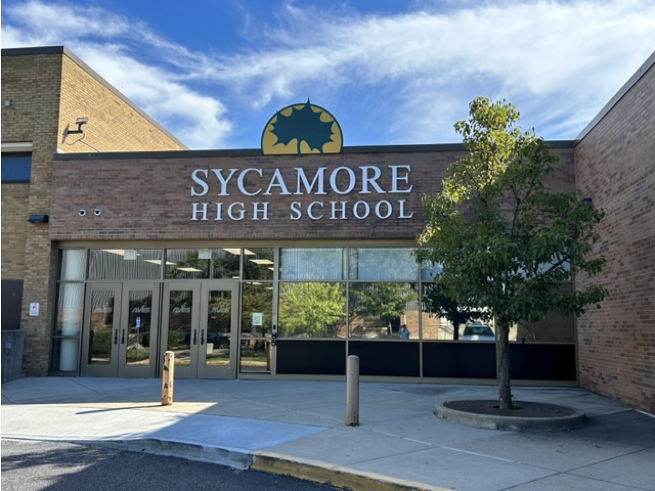 Brick school entrance with glass doors, school name sign, and leaf logo above