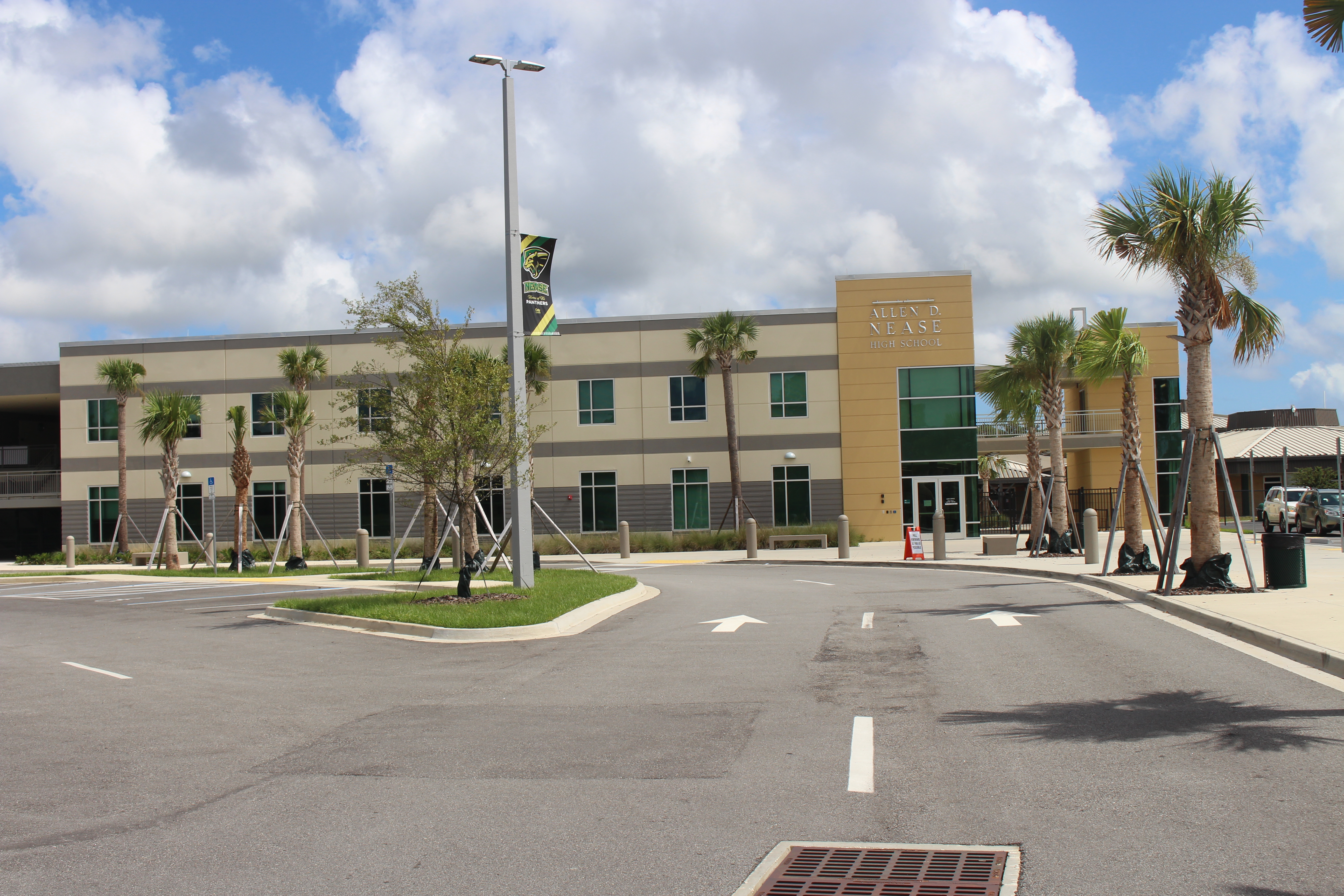 Two-story school building with palm trees and parking lot under a blue sky.