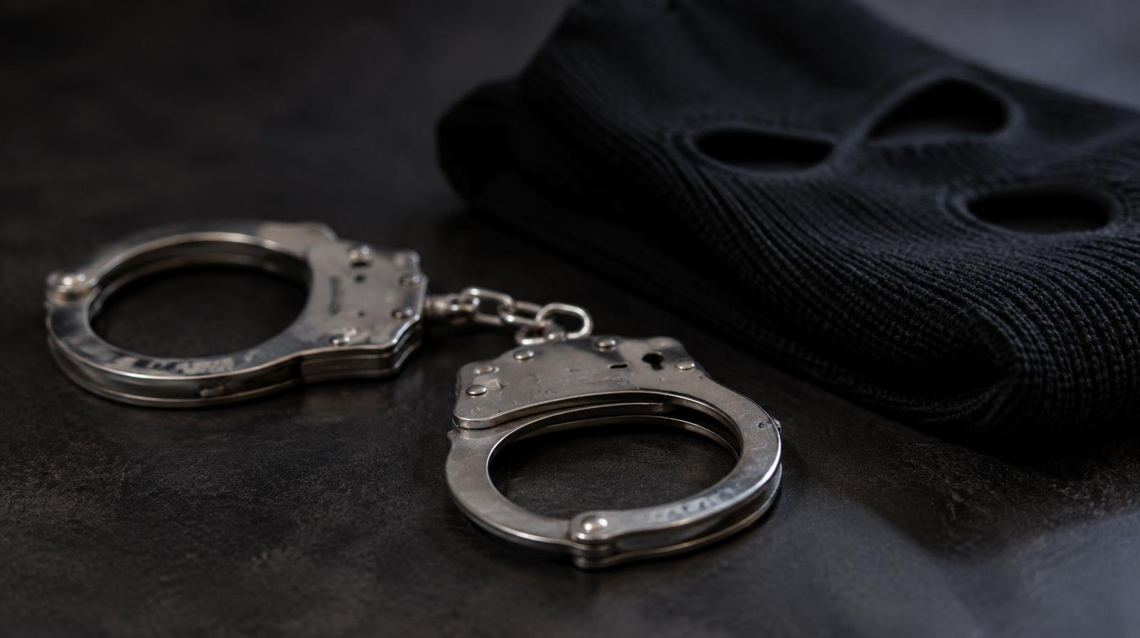 Steel handcuffs resting on a dark surface beside a folded black ski mask.
