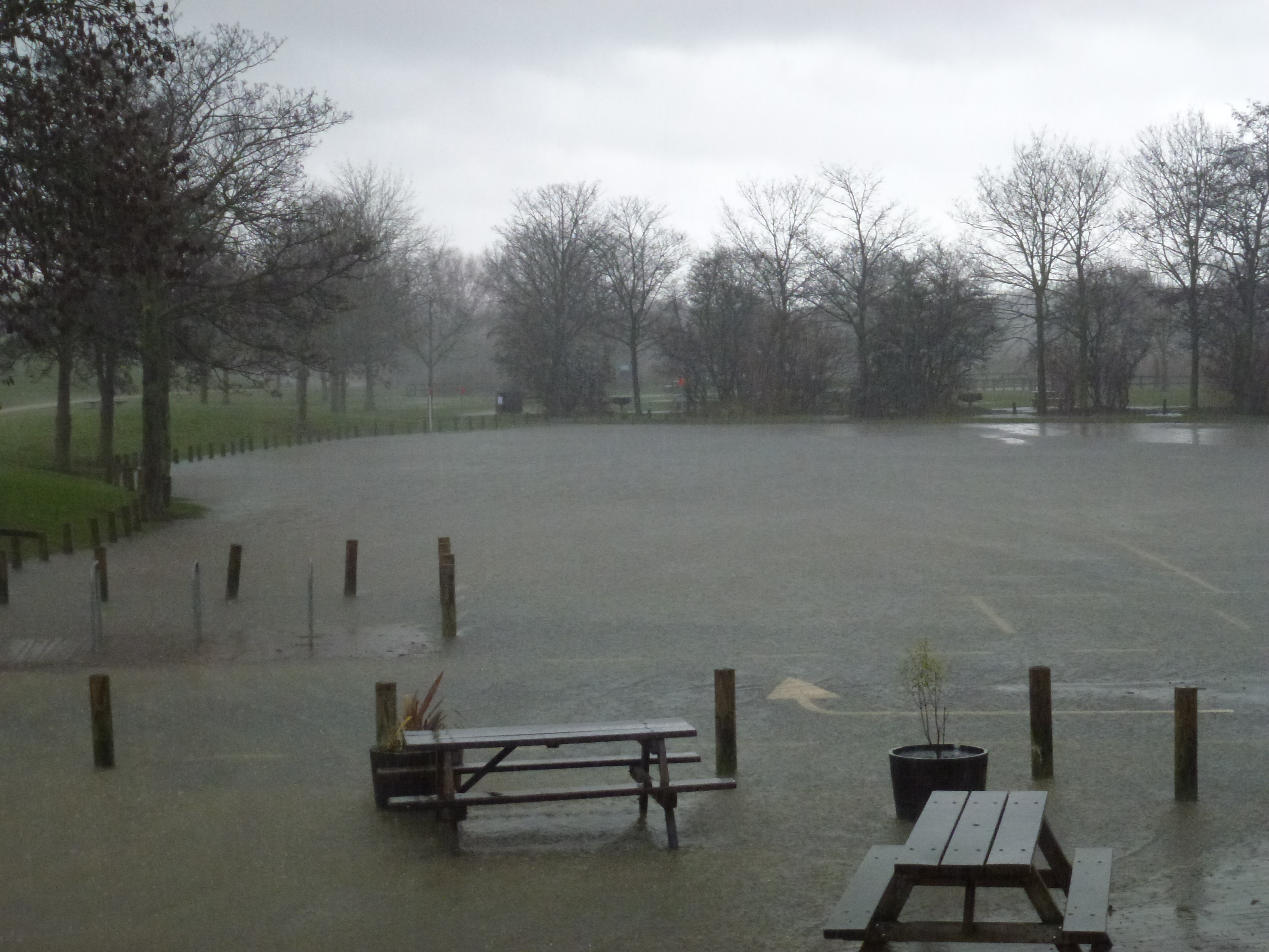Flooded outdoor area with picnic tables partially submerged in standing water under overcast skies.