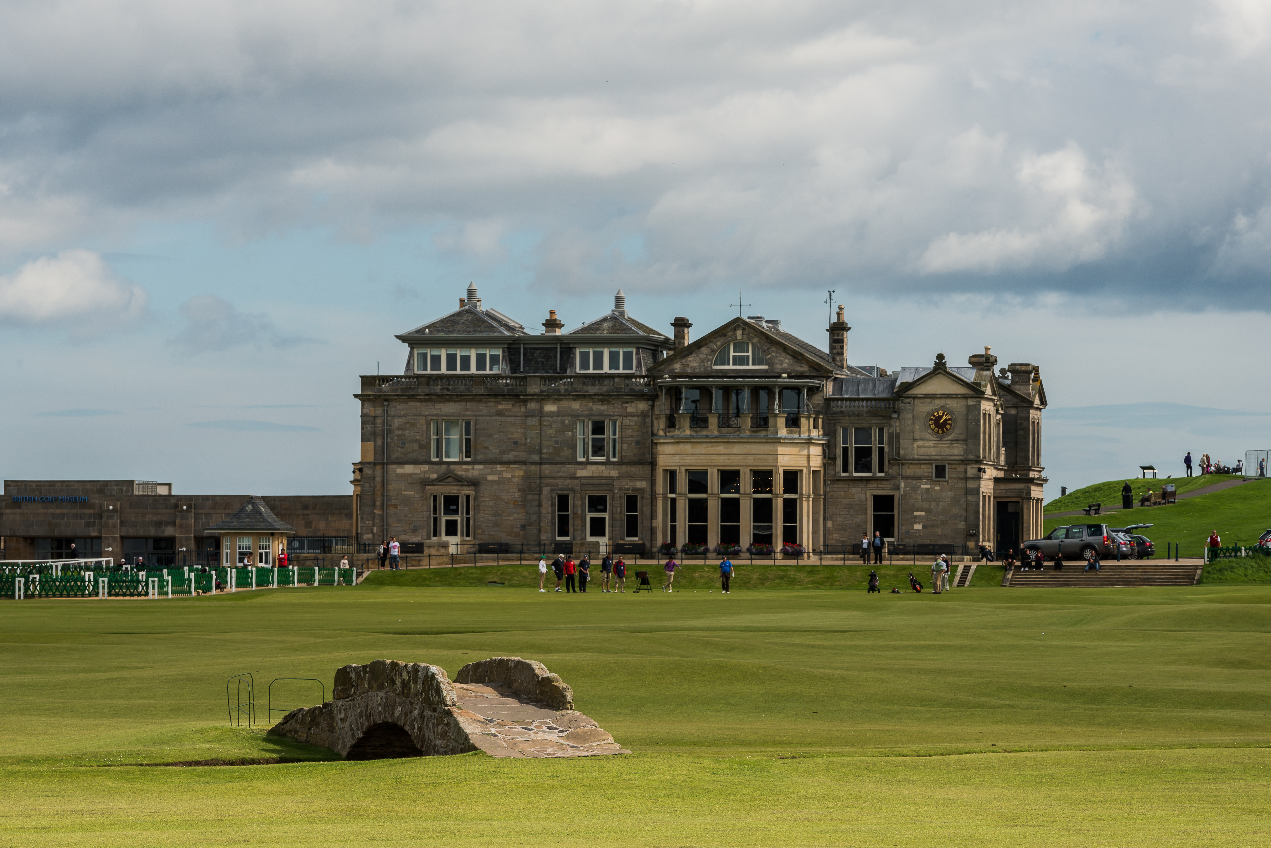 Stone bridge over a burn on a links fairway with a large clubhouse behind.