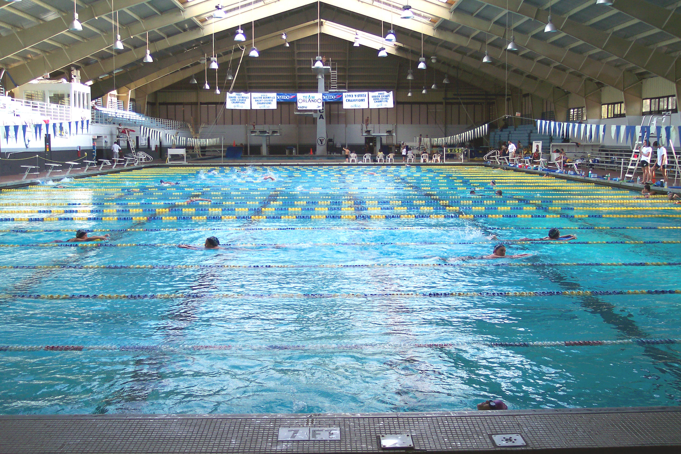 Indoor swimming pool with blue and yellow lane dividers and swimmers in the water.