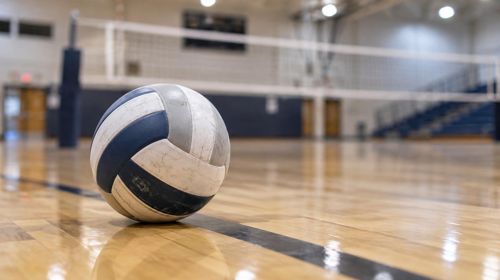 A volleyball resting on a hardwood gym floor with a net visible in the background.