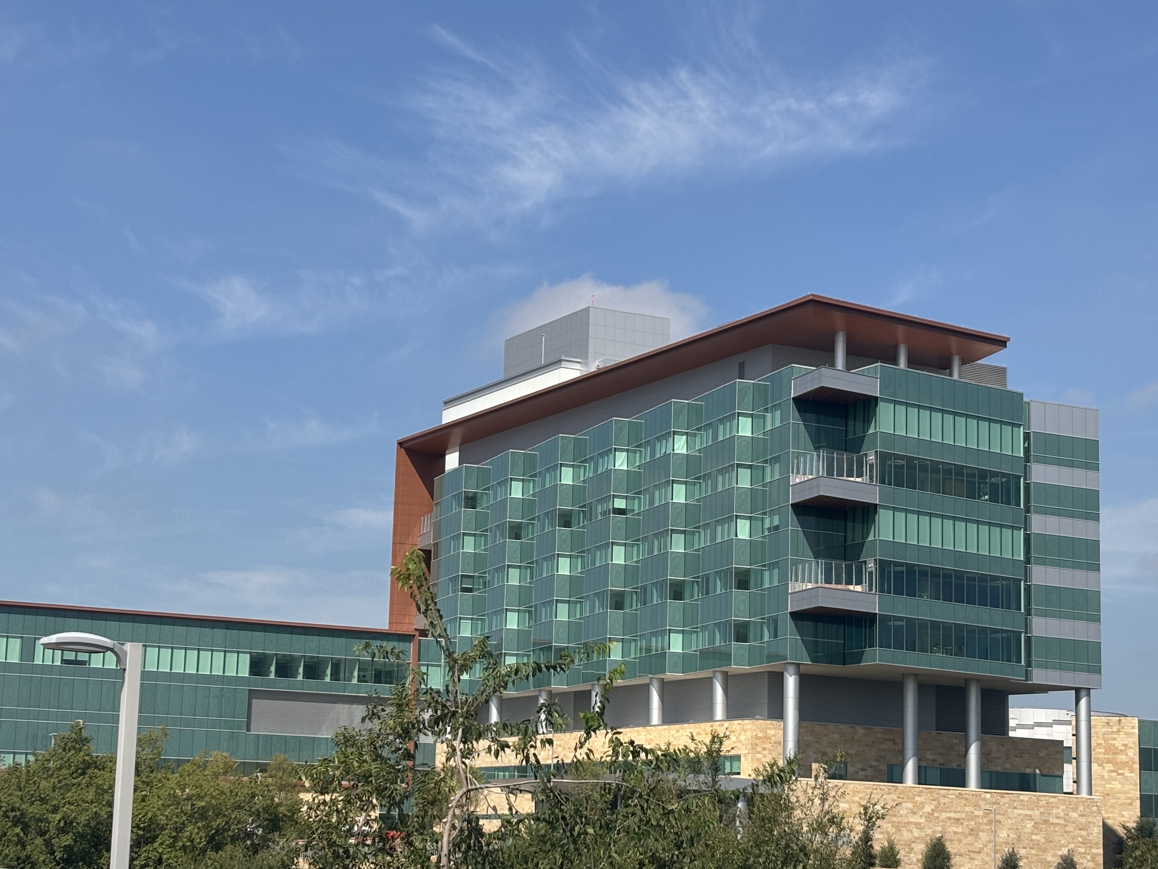 Multi-story hospital building with green glass facade and red-brown upper section.