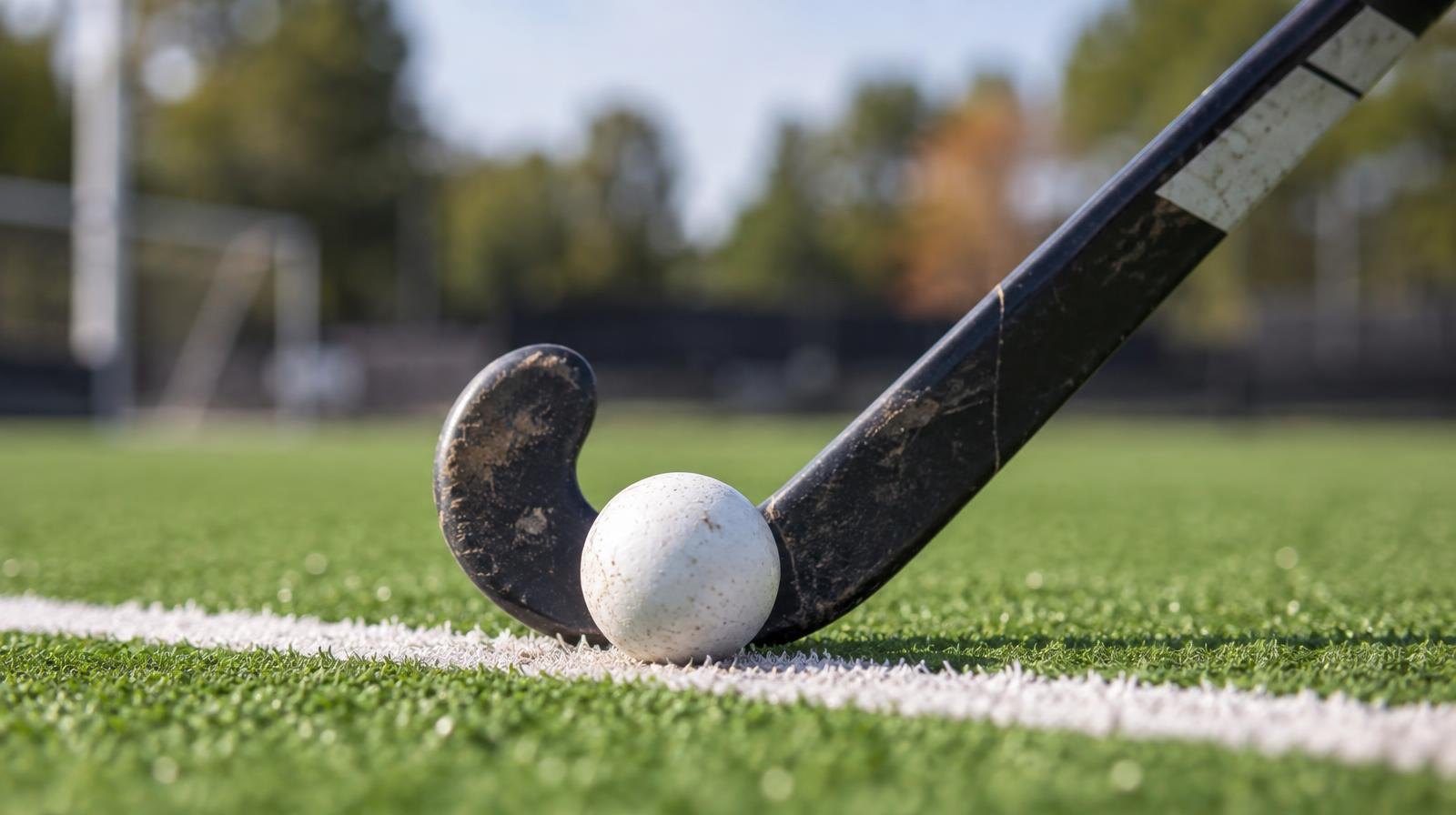 A field hockey stick and ball resting on green artificial turf near a white line.