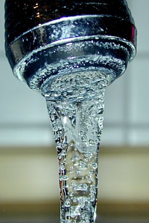 Water flowing from a chrome faucet with visible bubbles in the stream