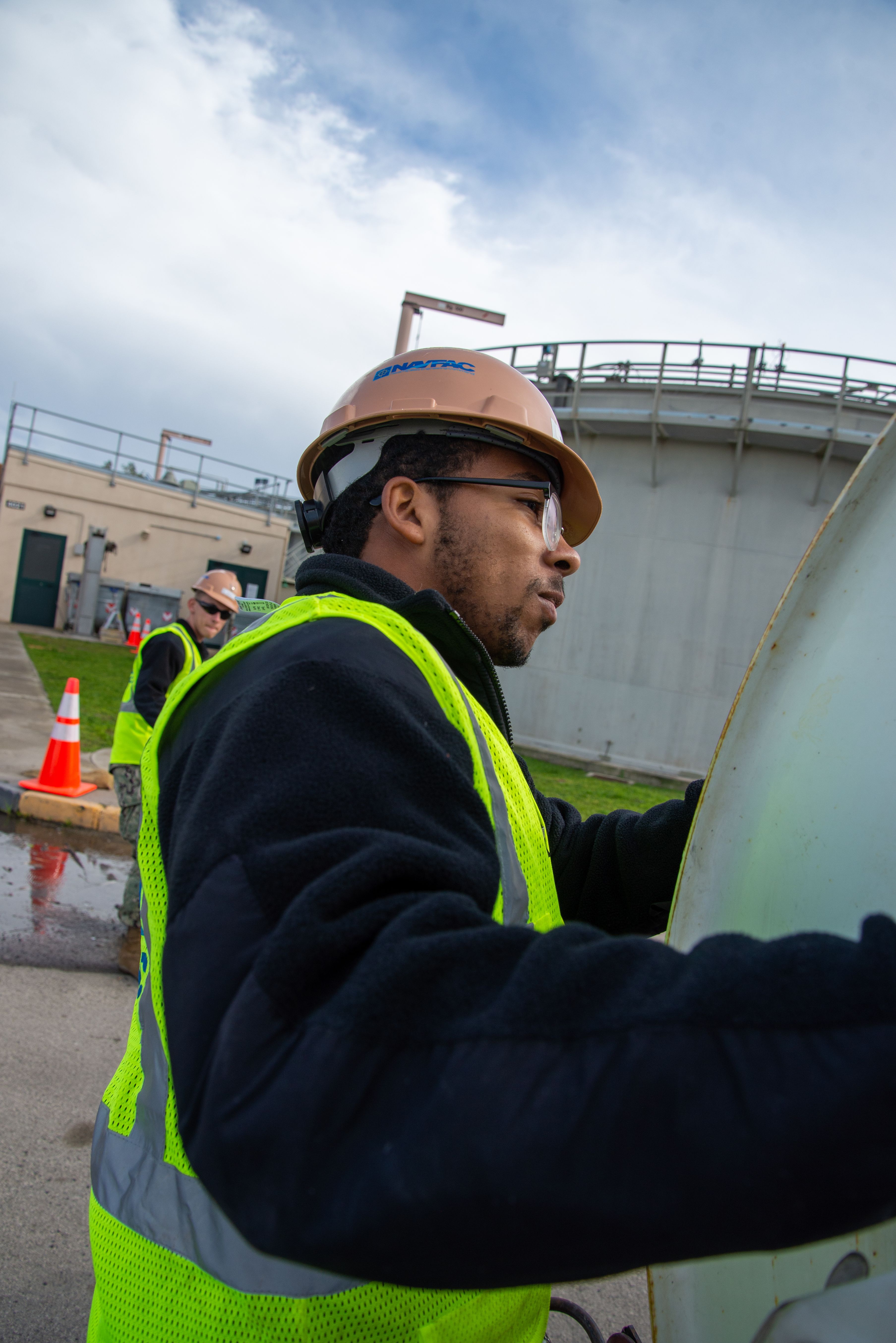 Two workers in hard hats and safety vests handle equipment at a water facility.