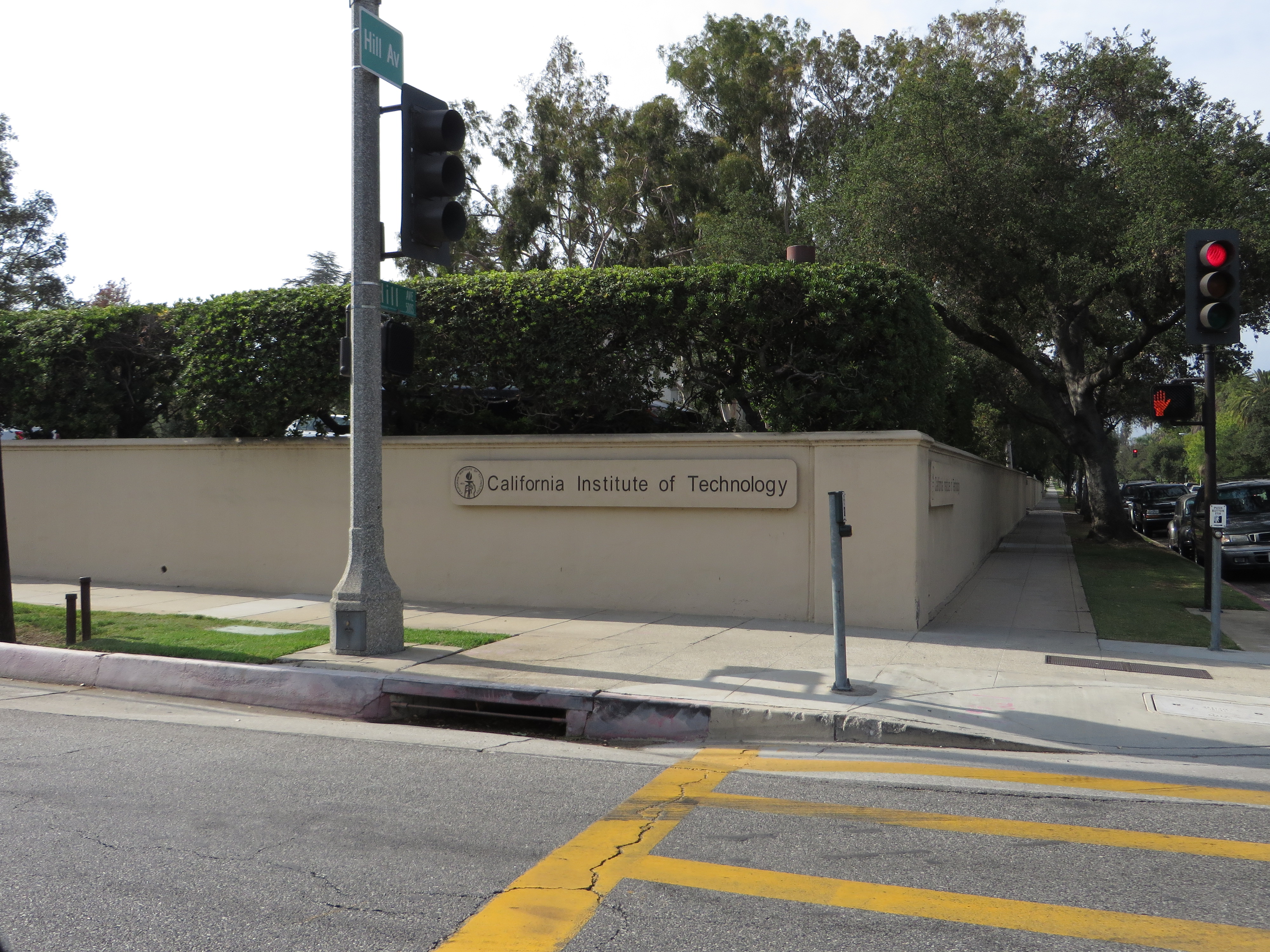 Stone perimeter wall bearing the California Institute of Technology name, with hedges and traffic signals.