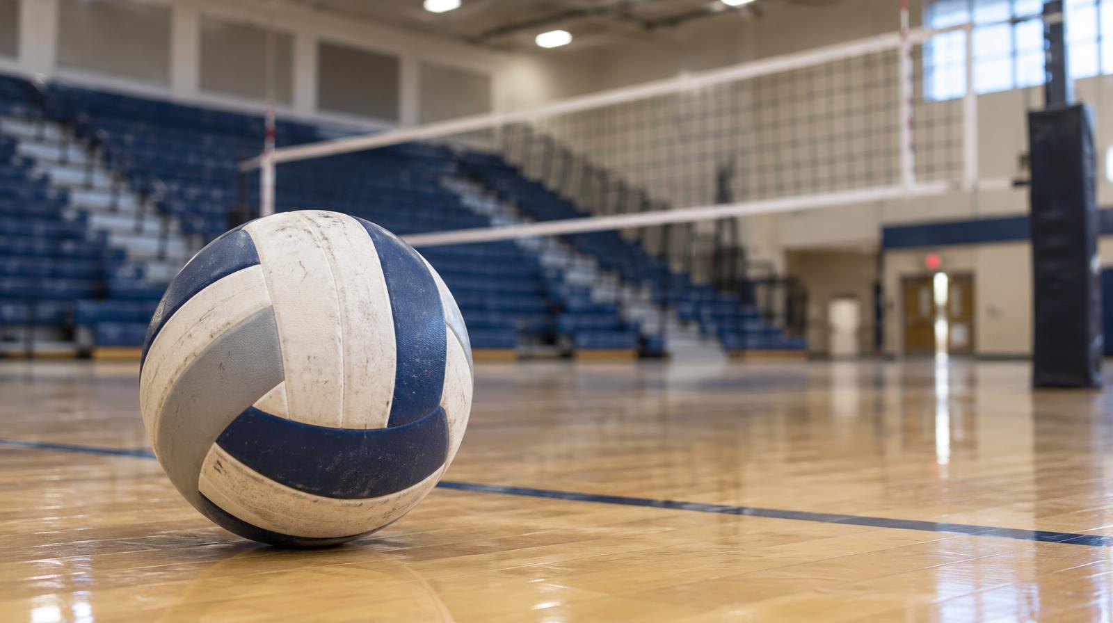 A volleyball resting on a hardwood gymnasium floor near a net.