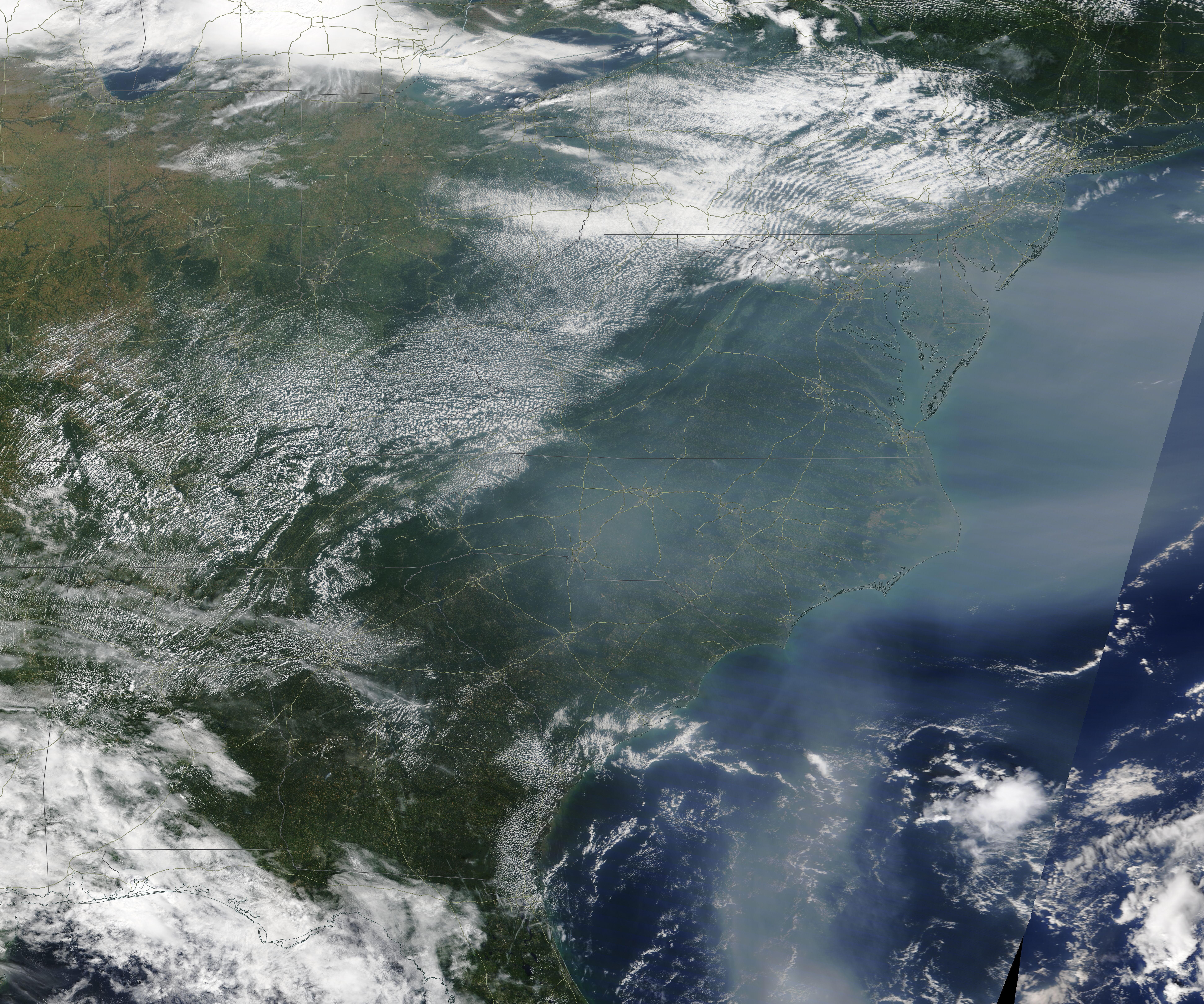 Satellite view showing thick gray wildfire smoke haze blanketing a large region of the United States.