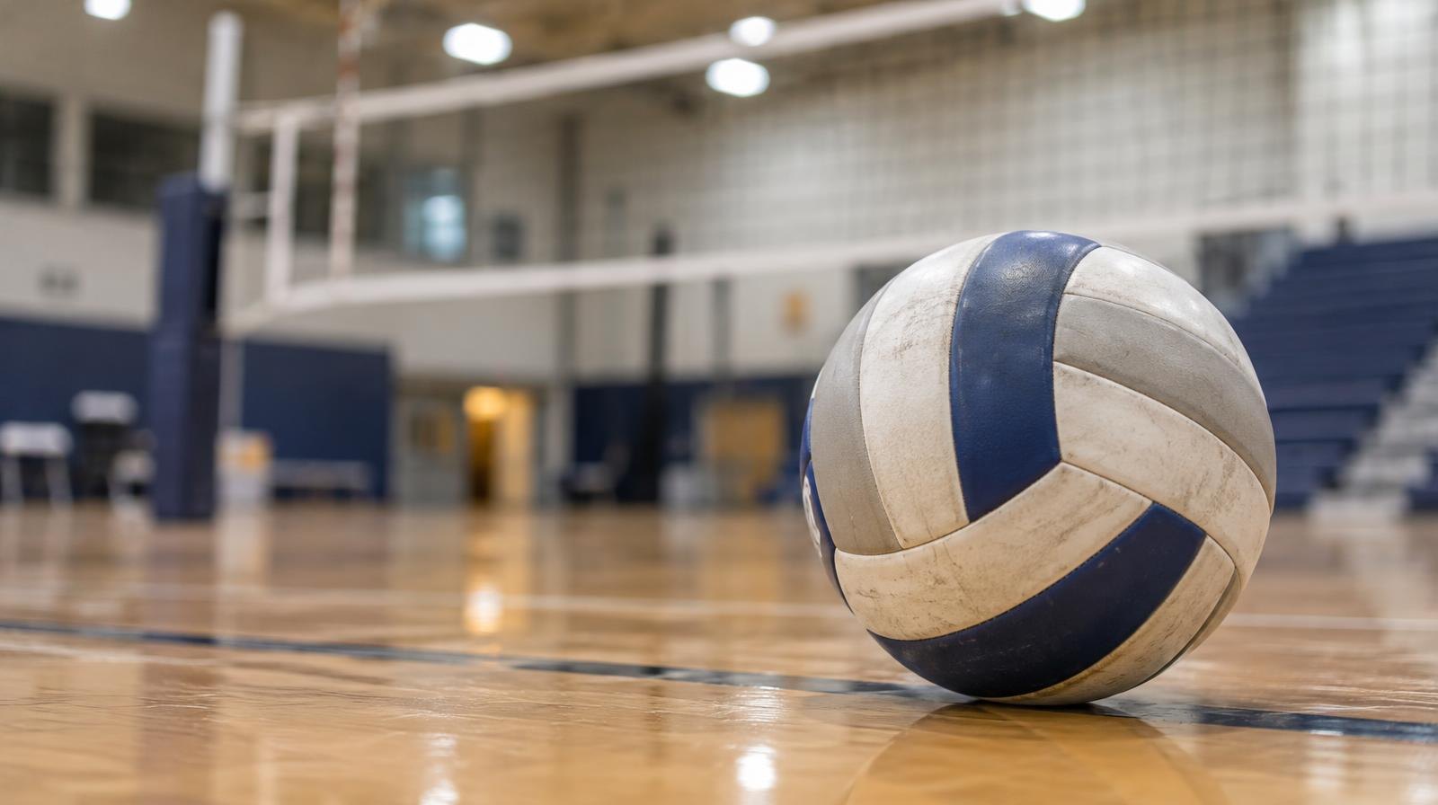 A volleyball sitting on a hardwood gymnasium floor near the net.