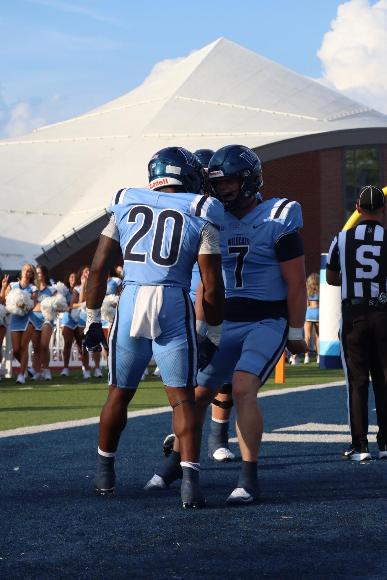 Two football players in light blue uniforms embrace on the field after a game.