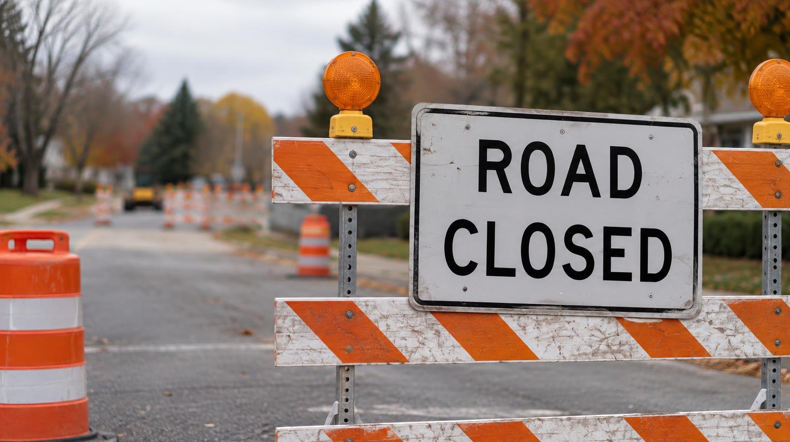 Orange-and-white striped traffic barricades with a Road Closed sign on a suburban street.