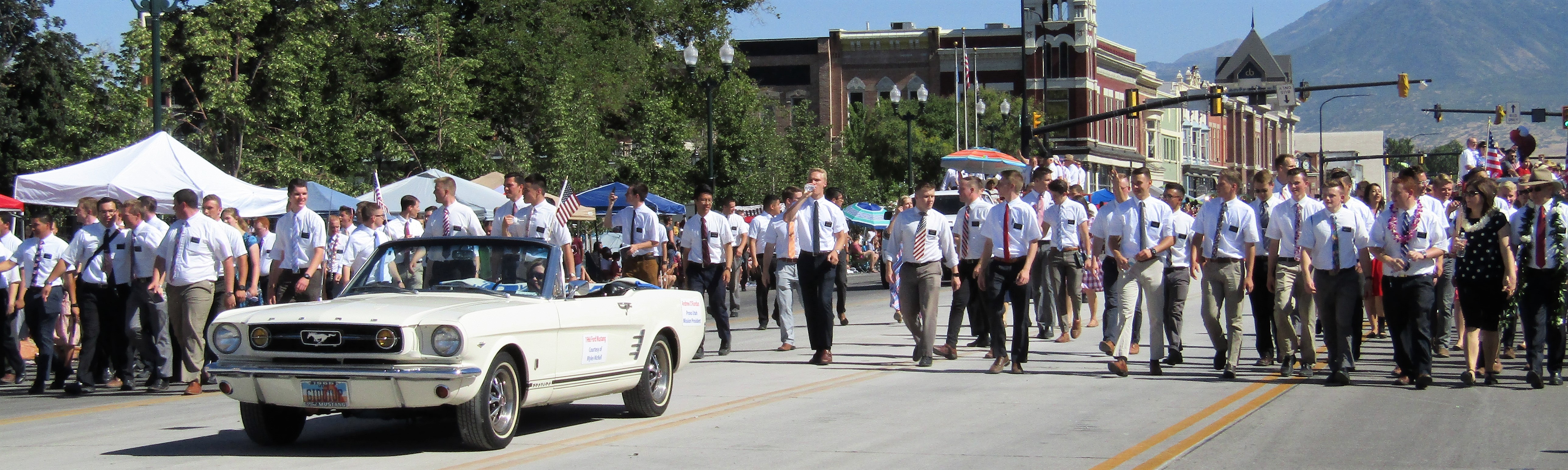 Large group of young men in white shirts and ties marching in a parade with mountains in the background.
