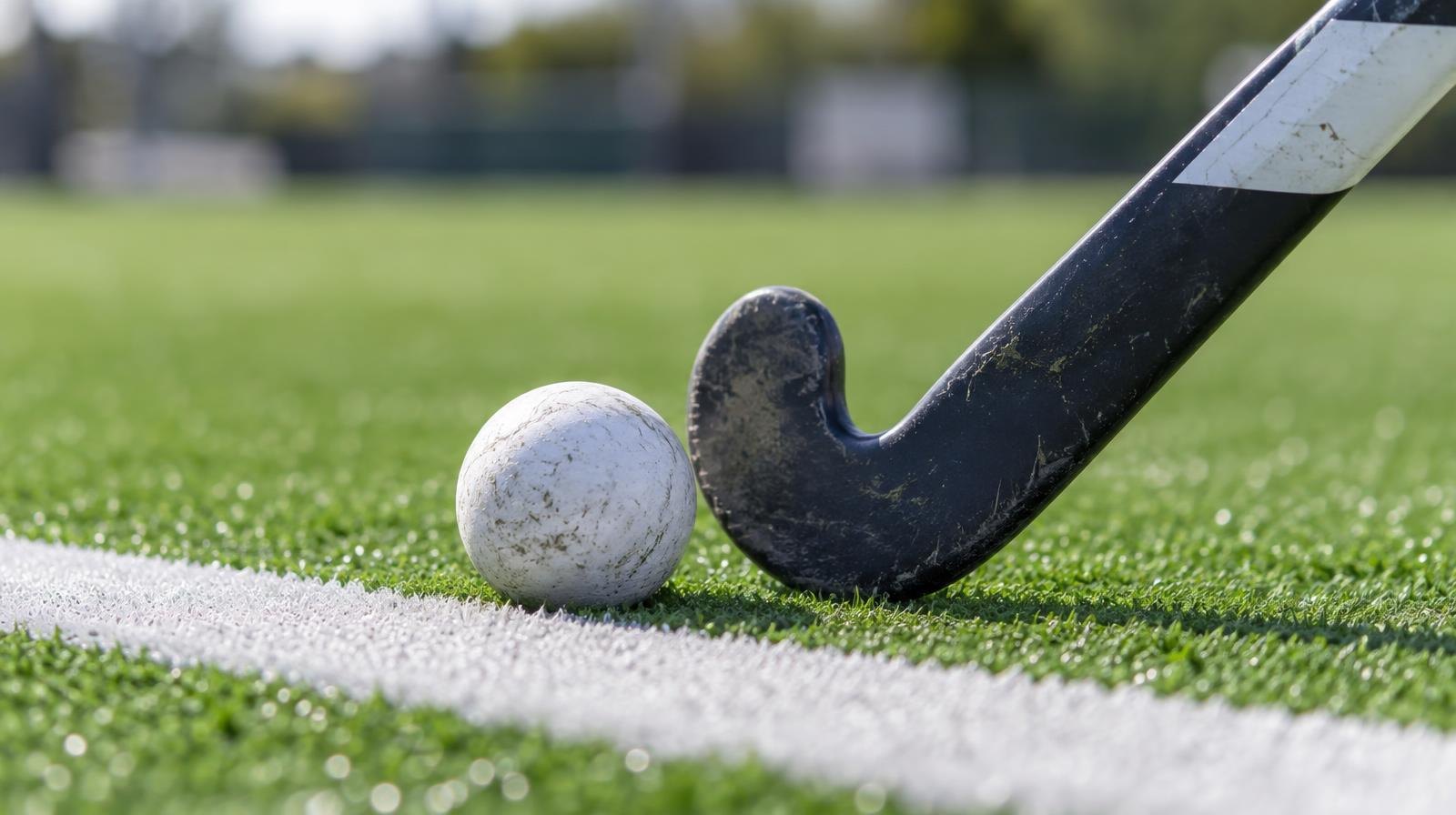 A field hockey stick and ball resting on green artificial turf beside a white painted line.