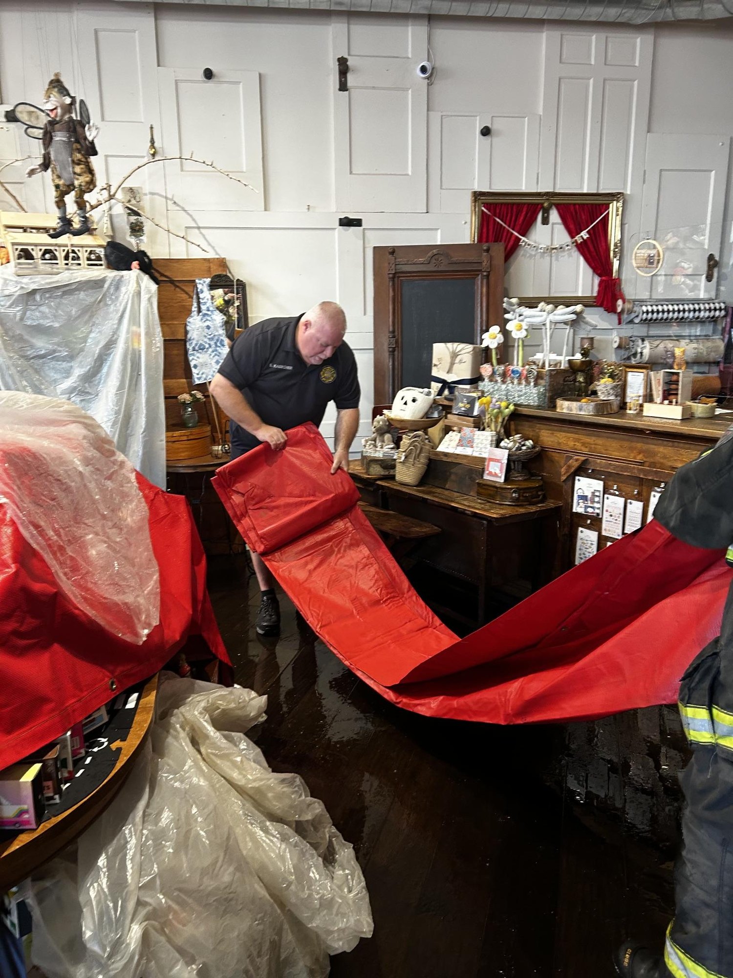 Firefighter unfolds a large red salvage tarp on a wet retail shop floor.