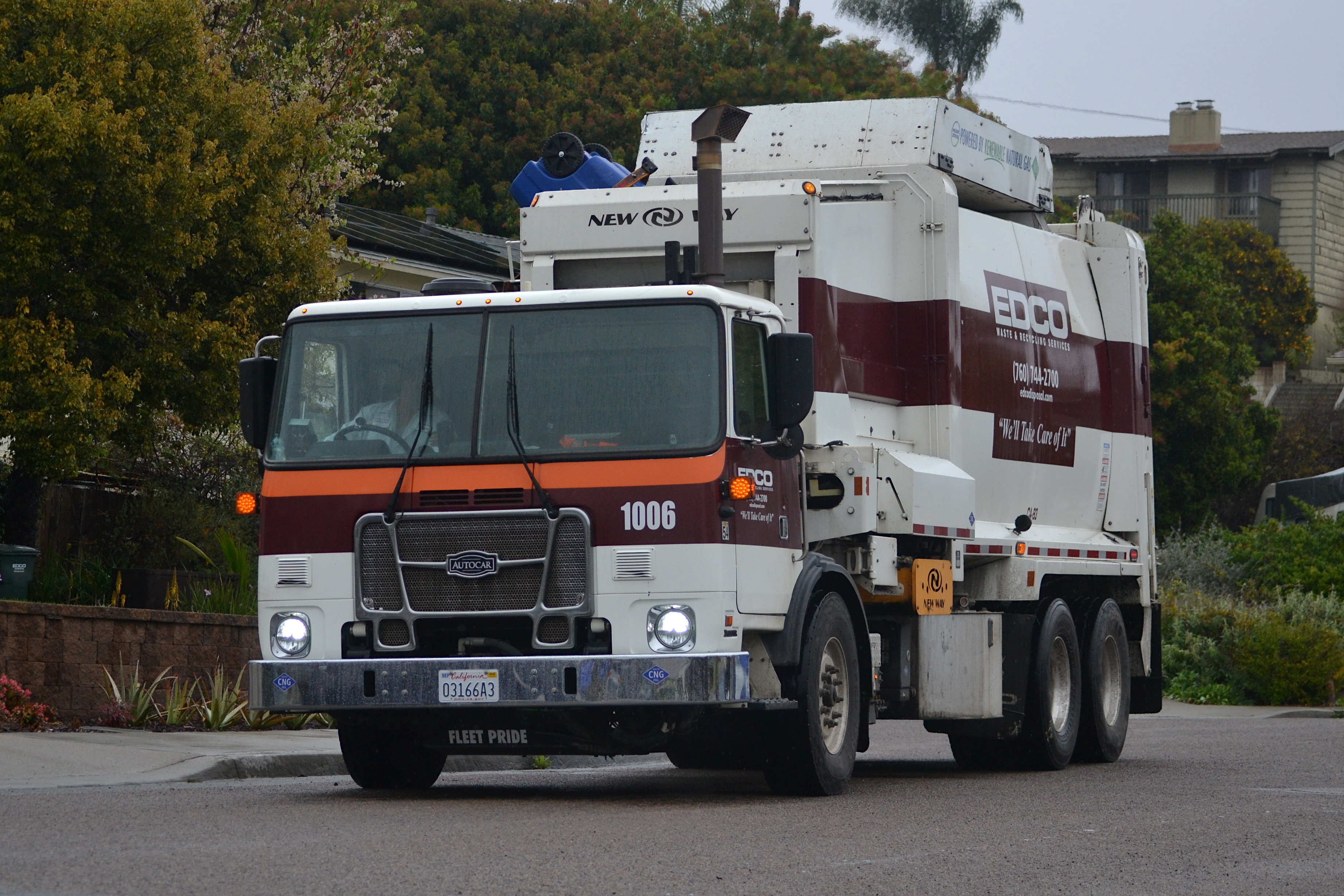 White and maroon automated side-loader recycling truck on a residential street.