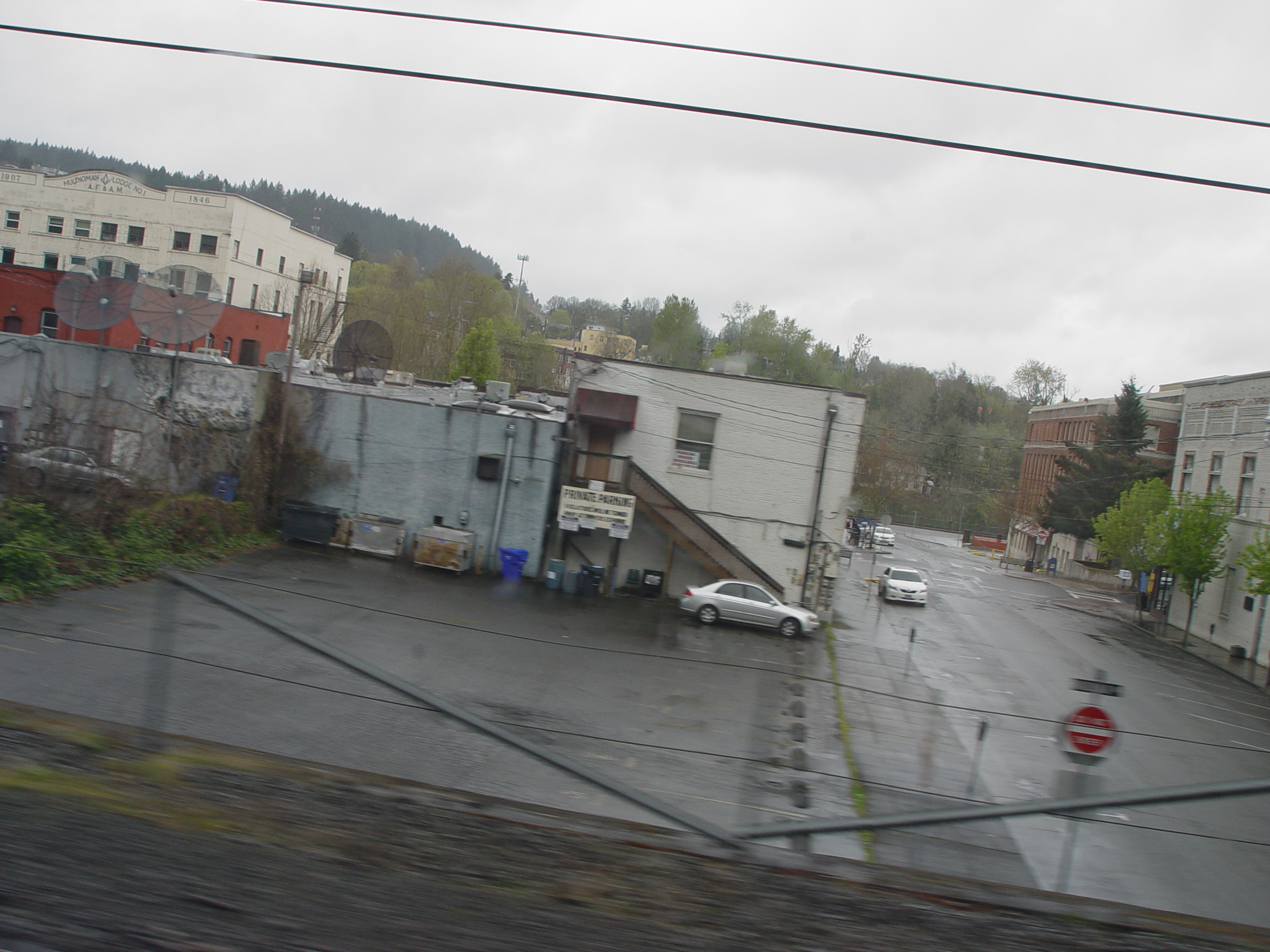 Rainy street scene in downtown Oregon City, Oregon, with older commercial buildings and hills in the background.