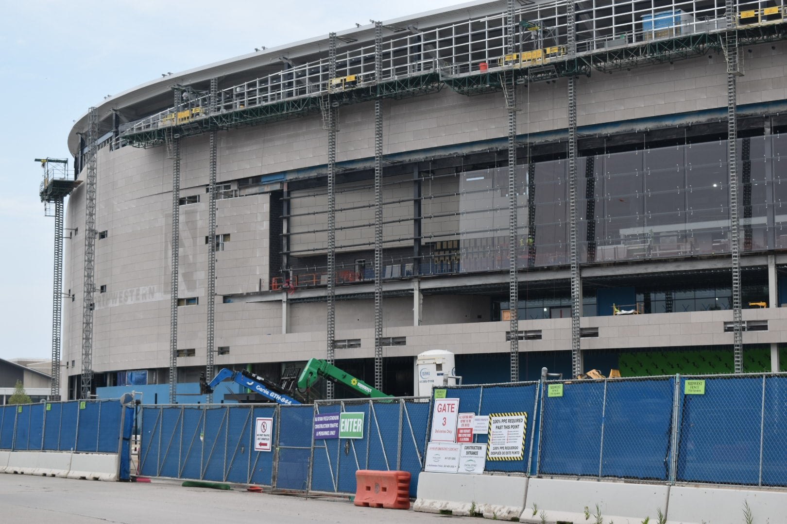 Large circular stadium under construction surrounded by blue fencing and a crane.