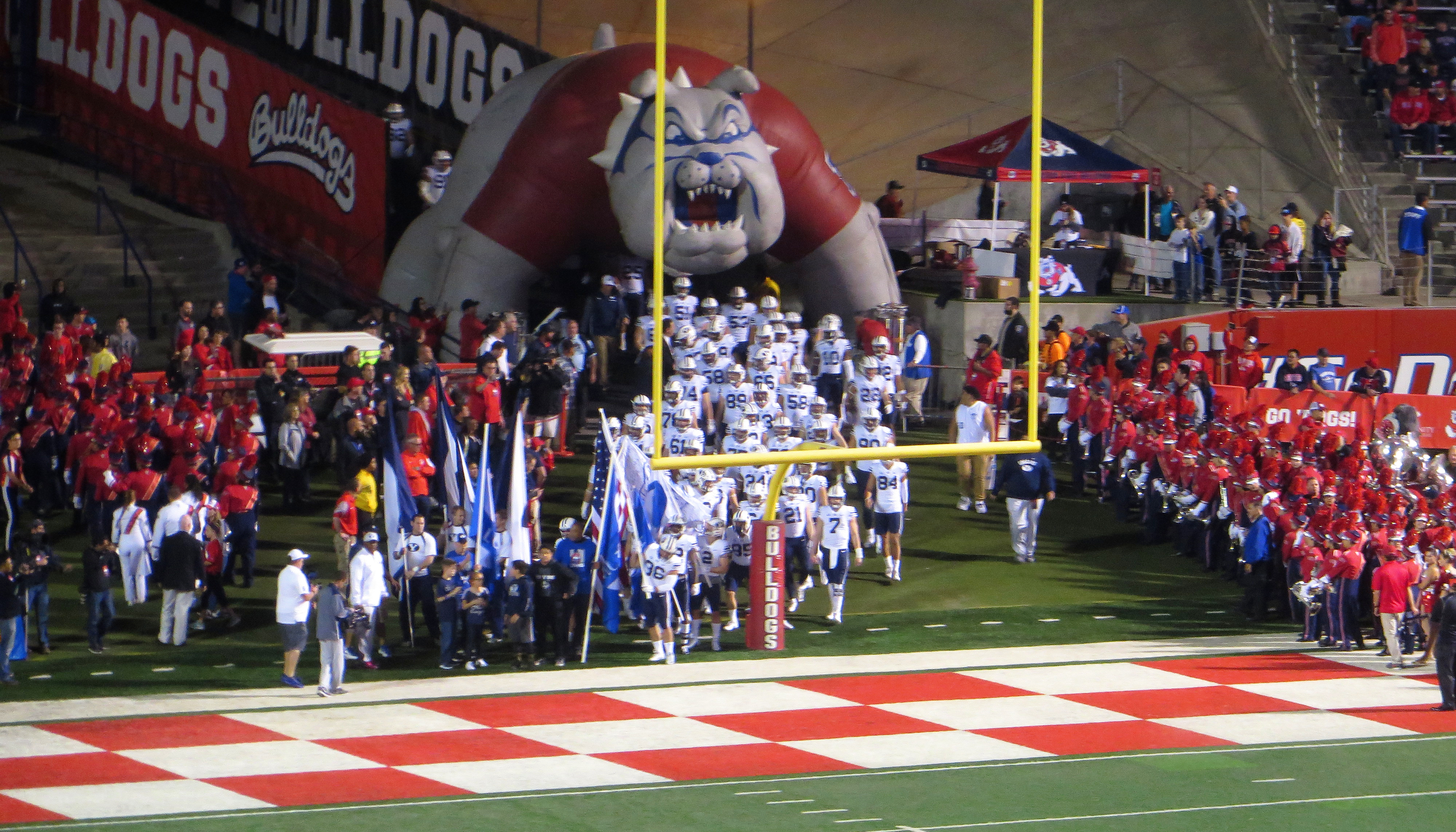 Football players run through an inflatable mascot tunnel onto a college football field.