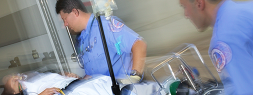Two paramedics in blue uniforms attend to a patient on a stretcher.
