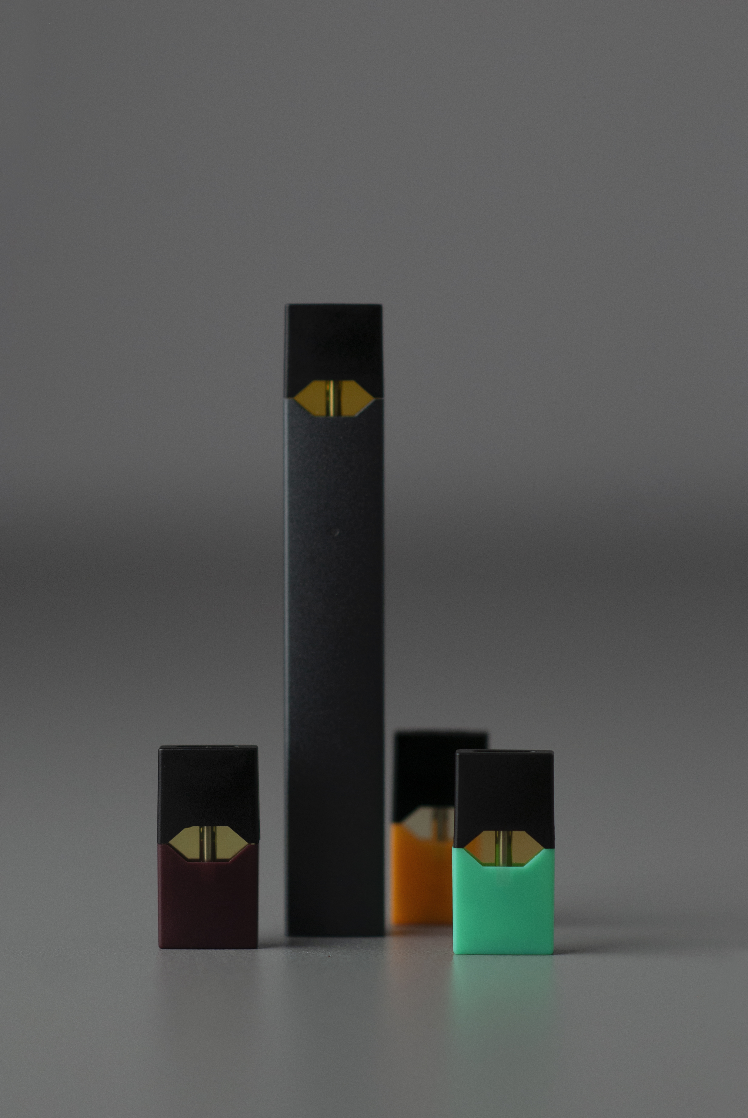 A slim black Juul vape device standing upright next to four colored pods.
