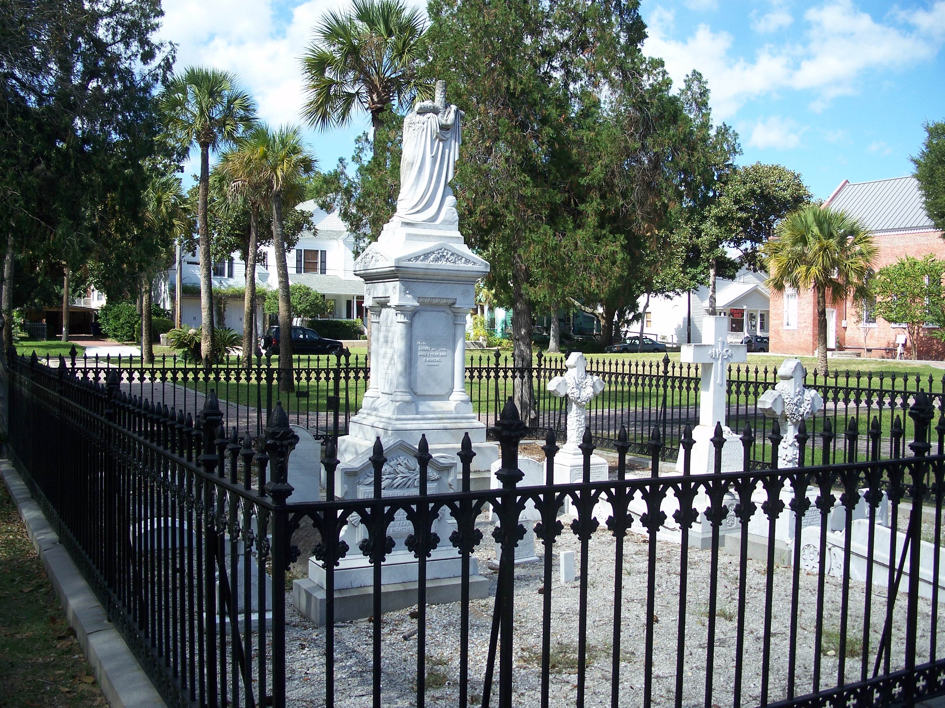 White marble funerary statue on a pedestal inside a wrought-iron fenced historic cemetery