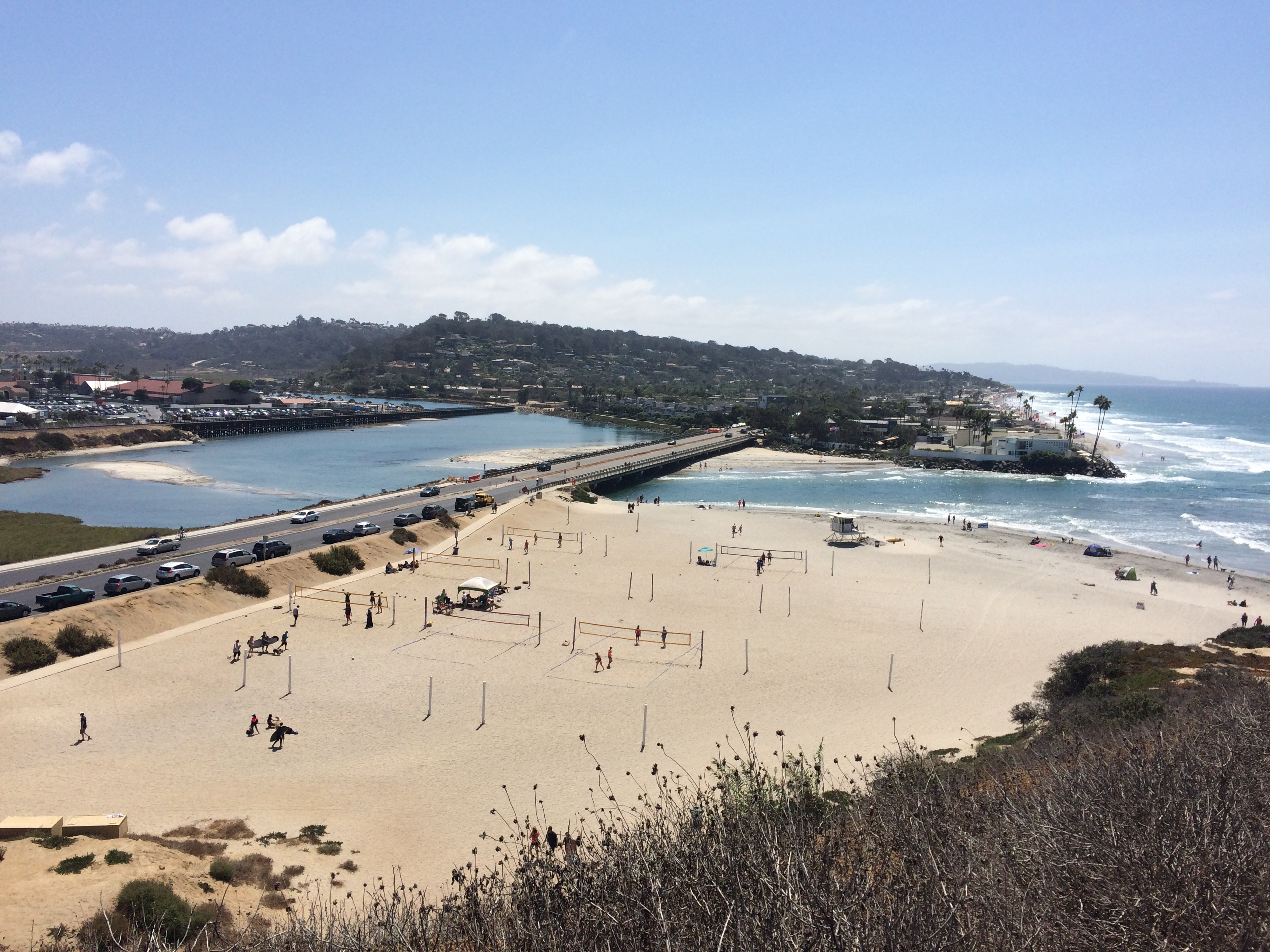 Aerial view of a bridge over a river lagoon near a sandy beach and ocean.