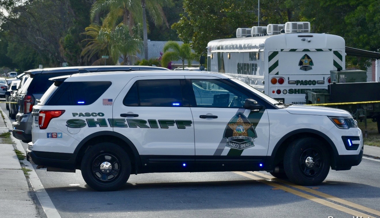 White Pasco Sheriff's Office SUV with blue emergency lights illuminated, parked on a street.