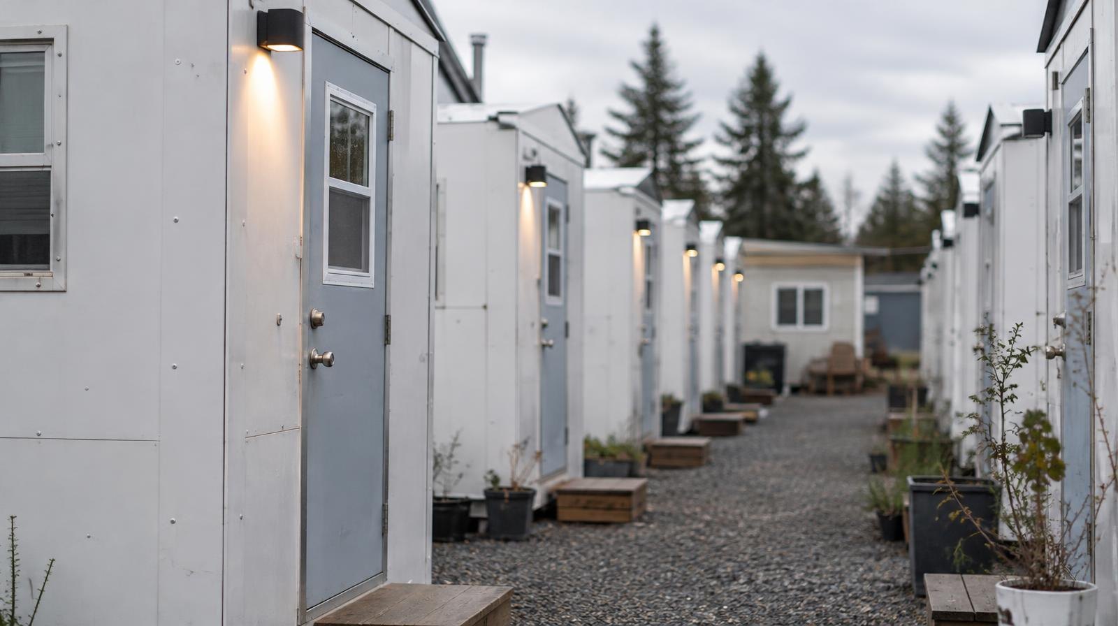 Row of small prefabricated shelter pods with individual doors along a gravel path.