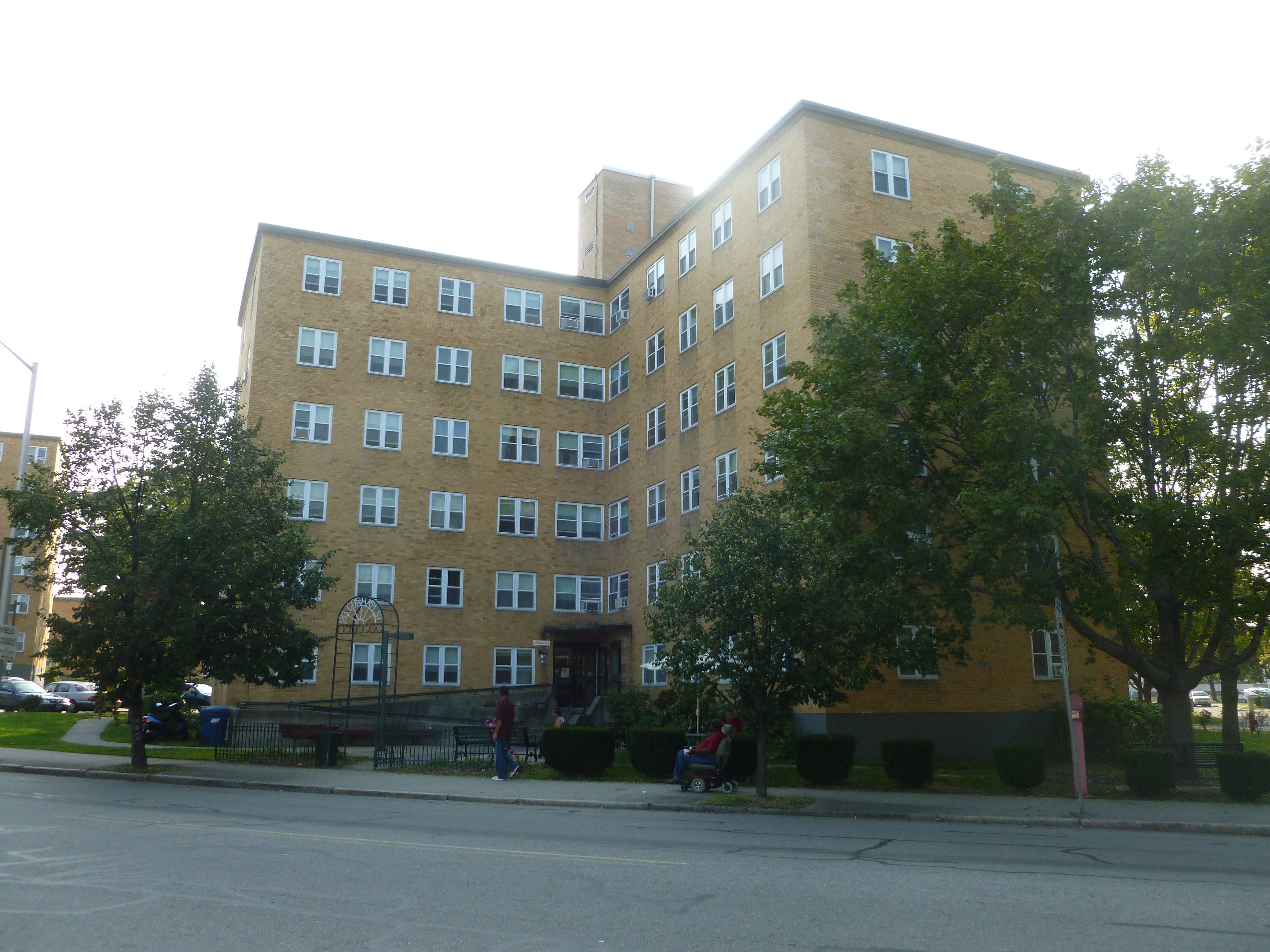Tall yellow brick apartment building with multiple windows and a central entrance.